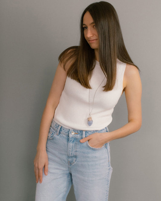 Woman wearing a white sleeveless top and light blue jeans against a gray background