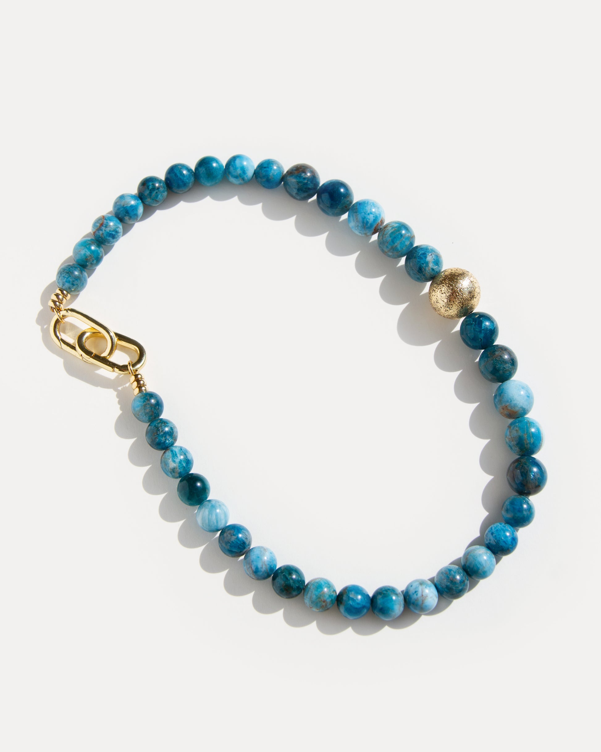 Ocean View Necklace 
Full, top-down view of the bold apatite beaded necklace, featuring large, captivating blue apatite stones and an eye-catching asymmetrical 18K gold-plated brass bead. The clasp design is visible, showcasing the necklace's full length and structure. This piece is an excellent choice for a unique statement, blending modern elegance with natural elements, suitable for any occasion where a distinctive and stylish accessory is desired.