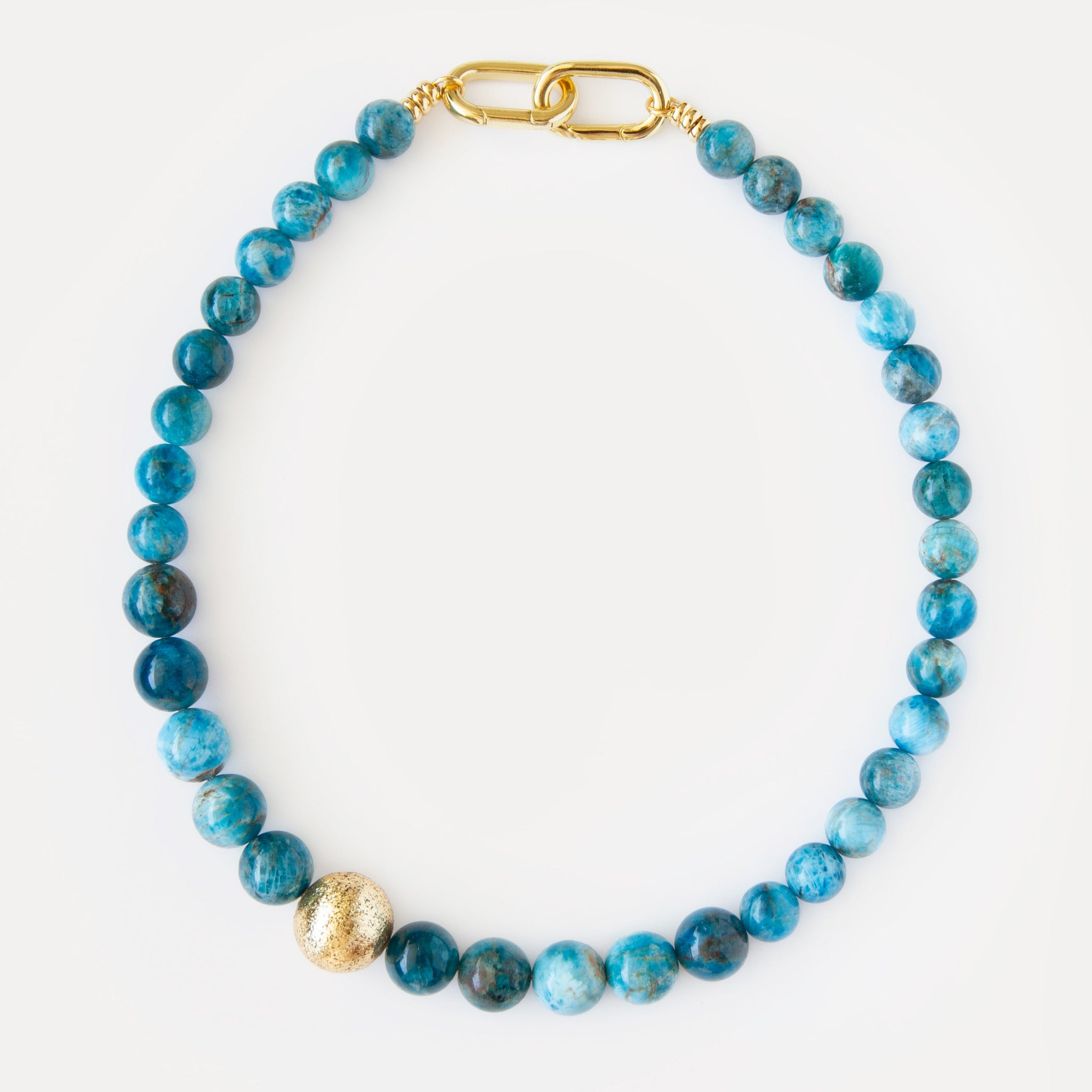 Ocean View Necklace 
Bold apatite beaded choker featuring large, vibrant blue apatite stones. It incorporates a unique, asymmetrically placed textured 18K gold-plated brass bead, adding a distinct contemporary accent. This statement jewelry piece elegantly combines natural beauty with modern design, perfect for special occasions, elevating everyday style, or as a thoughtful gift for discerning jewelry enthusiasts seeking timeless elegance.