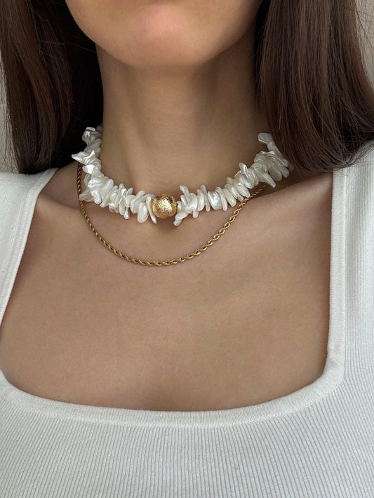 Festive Gold Necklace 
Close-up of a model wearing the luxurious layered necklace, clearly displaying the natural shell bead choker and the delicate 18K gold-plated brass chain. This view highlights the beautiful interplay of textures and the radiant glow on the skin, emphasizing its festive and elegant presence. Perfect for a statement piece at special events or adding a touch of luxury to daily wear.