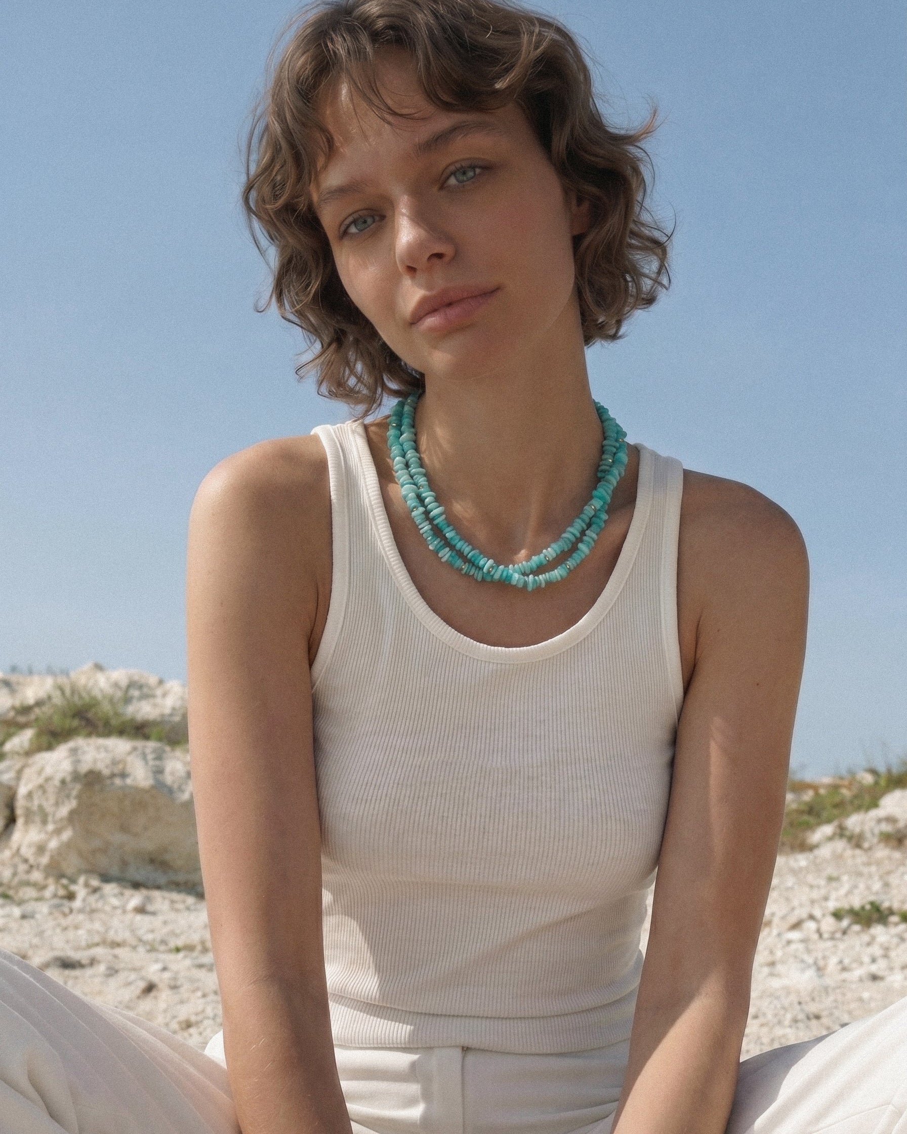 Model wearing a double strand amazonite necklace with turquoise beads, styled with a white top in soft summer light.