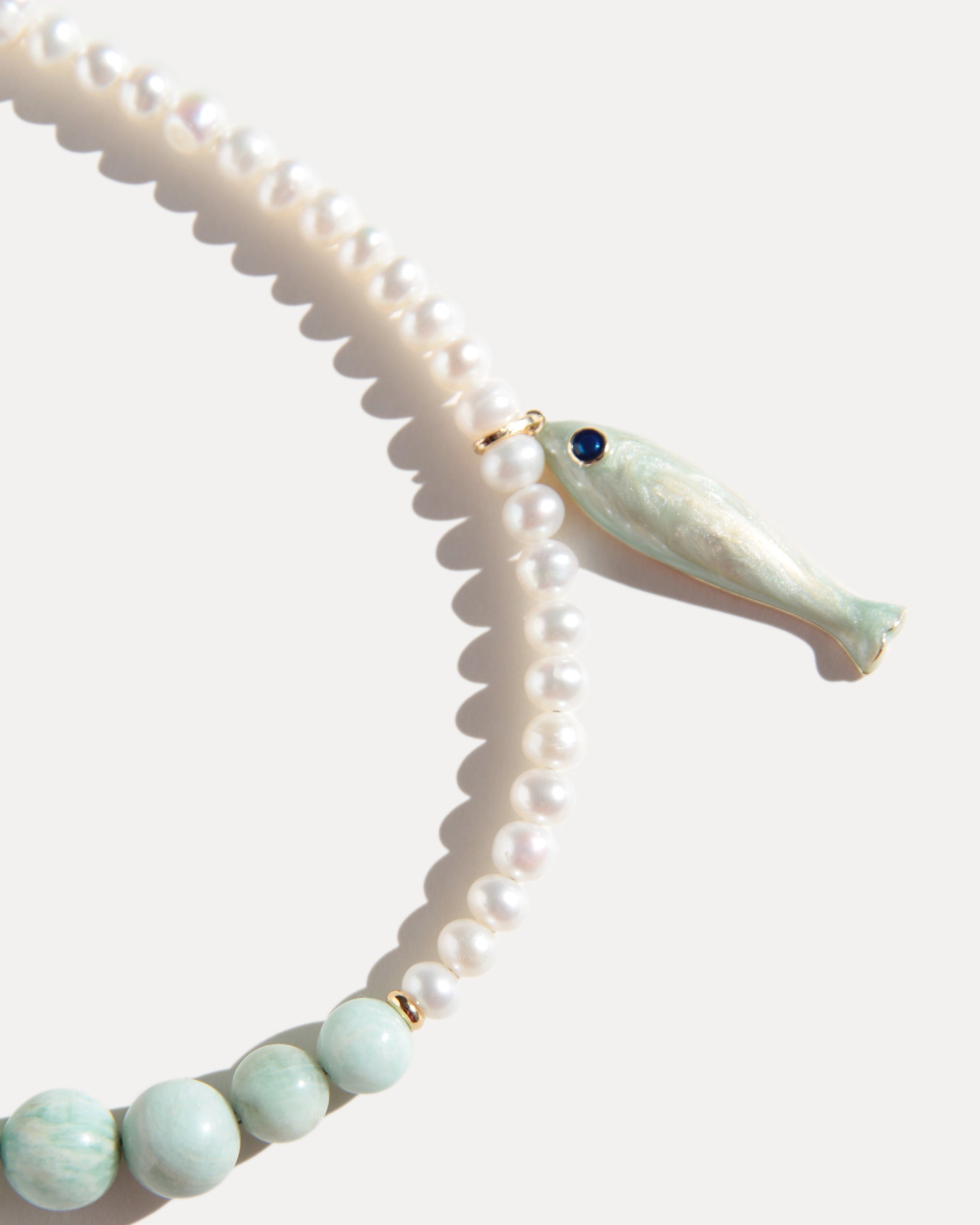 Close-up of freshwater pearl necklace with pale green amazonite beads and ceramic fish pendant in soft natural light