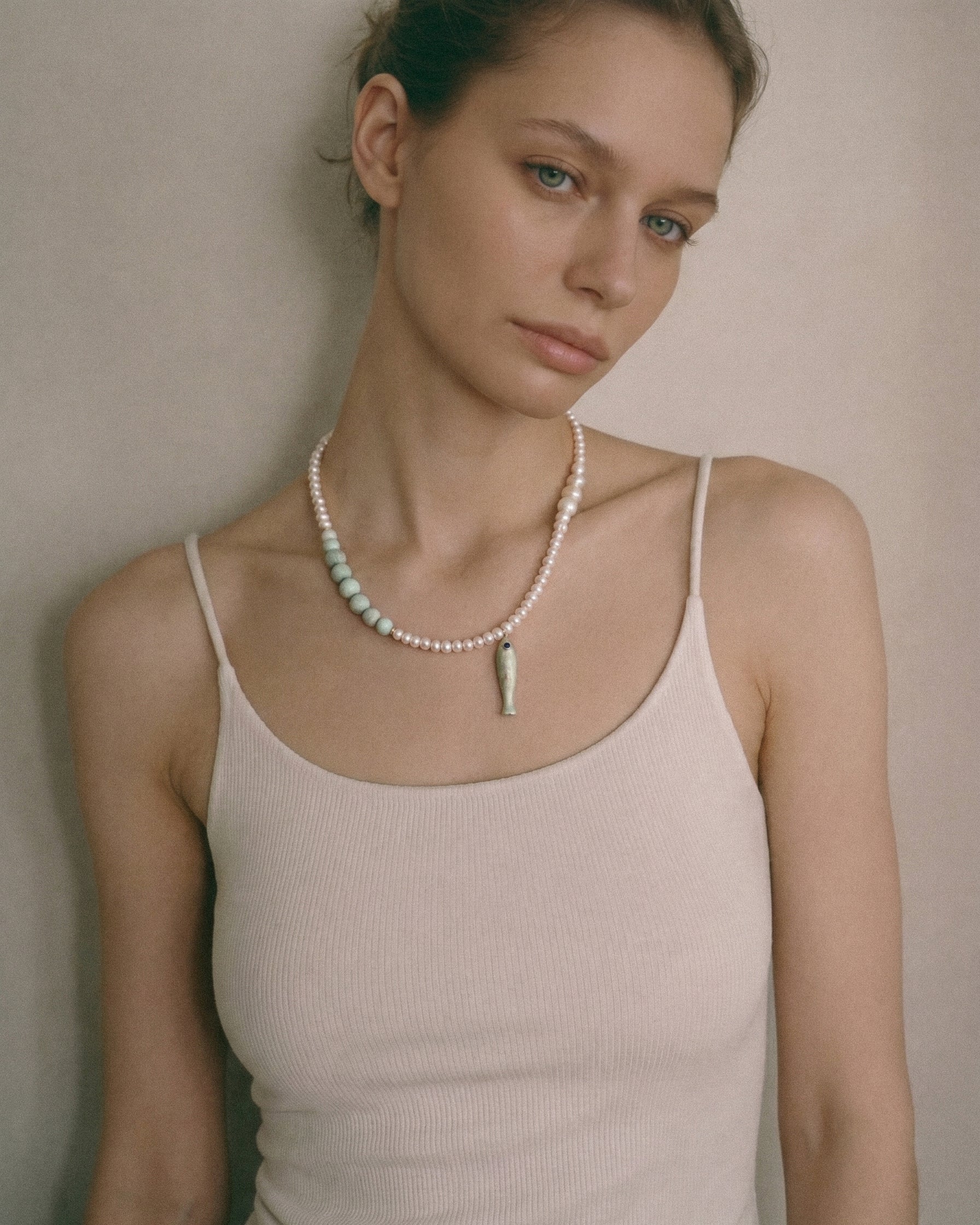 woman wearing freshwater pearl necklace with pale amazonite beads and ceramic fish pendant in soft editorial portrait