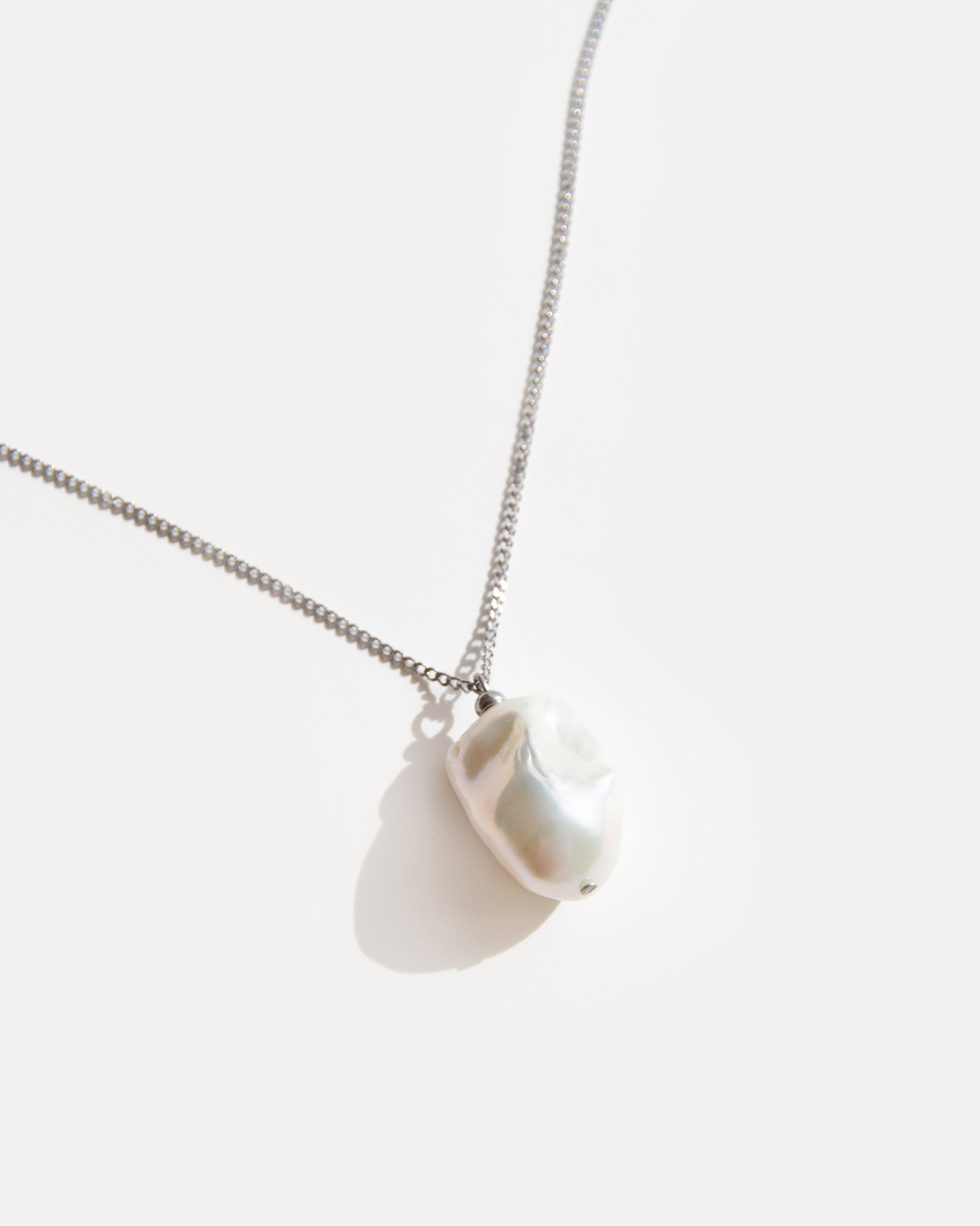 Close-up of baroque freshwater pearl pendant on stainless steel chain, highlighting its organic shape and natural iridescent glow.