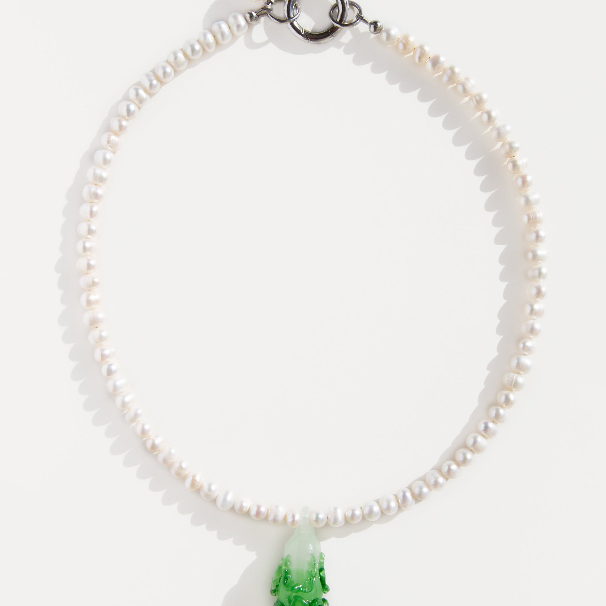Freshwater pearl necklace with a green lampwork bok choy pendant and stainless steel clasp – minimal flat lay on white background.