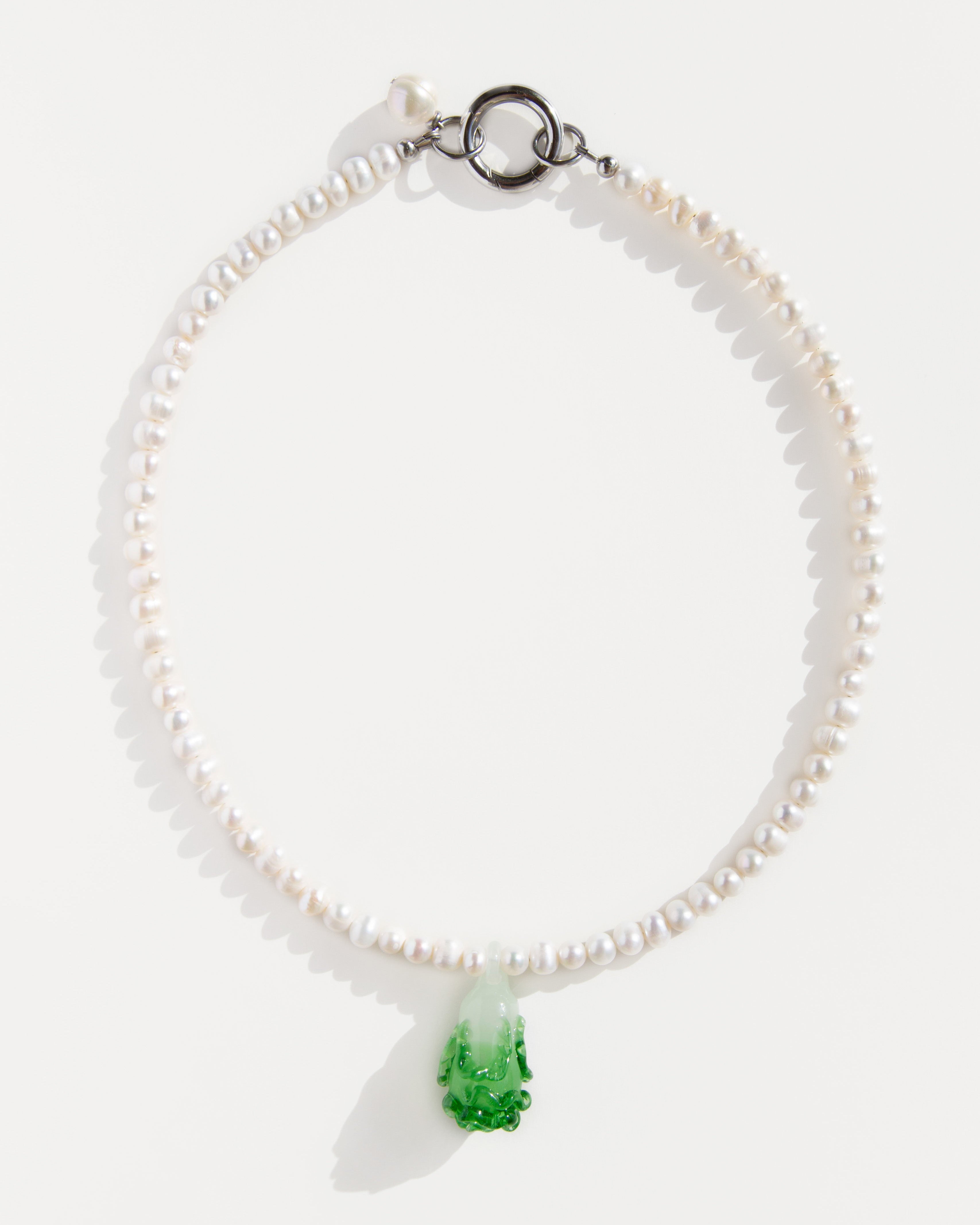 Freshwater pearl necklace with a green lampwork bok choy pendant and stainless steel clasp – minimal flat lay on white background.