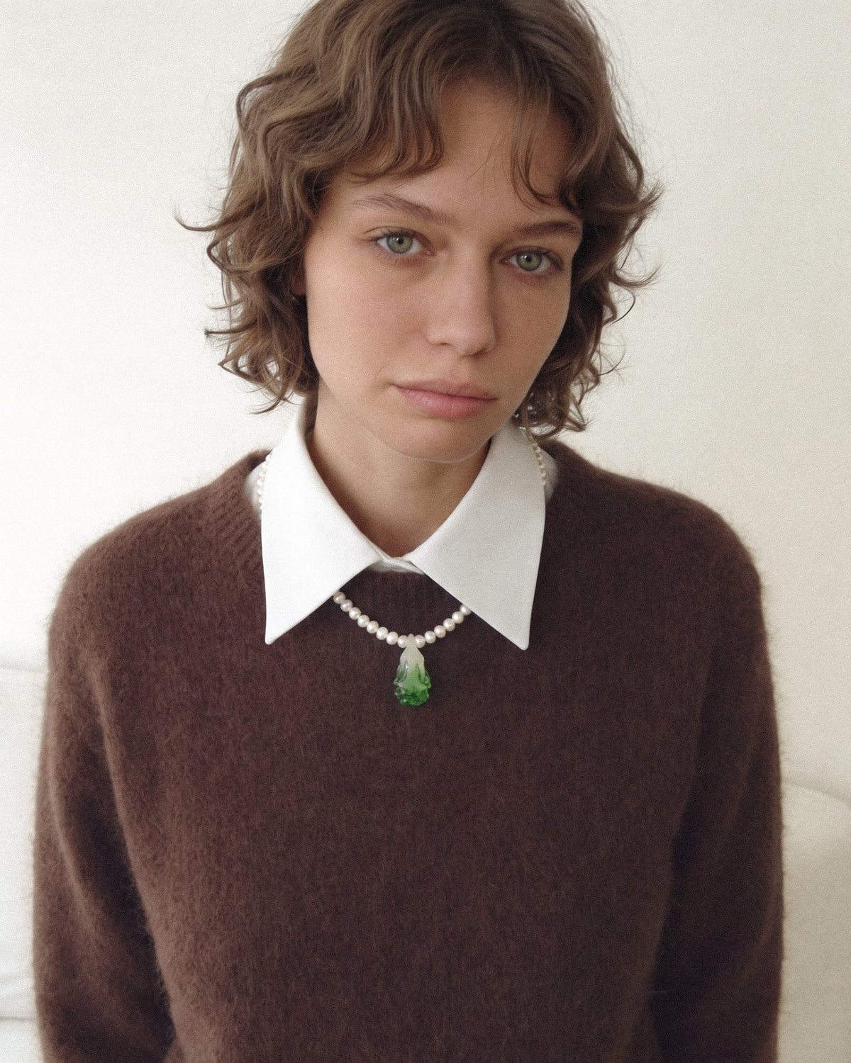 Model wearing a freshwater pearl necklace with a green glass bok choy pendant over a brown sweater.