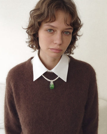 Model wearing a freshwater pearl necklace with a green glass bok choy pendant over a brown sweater.