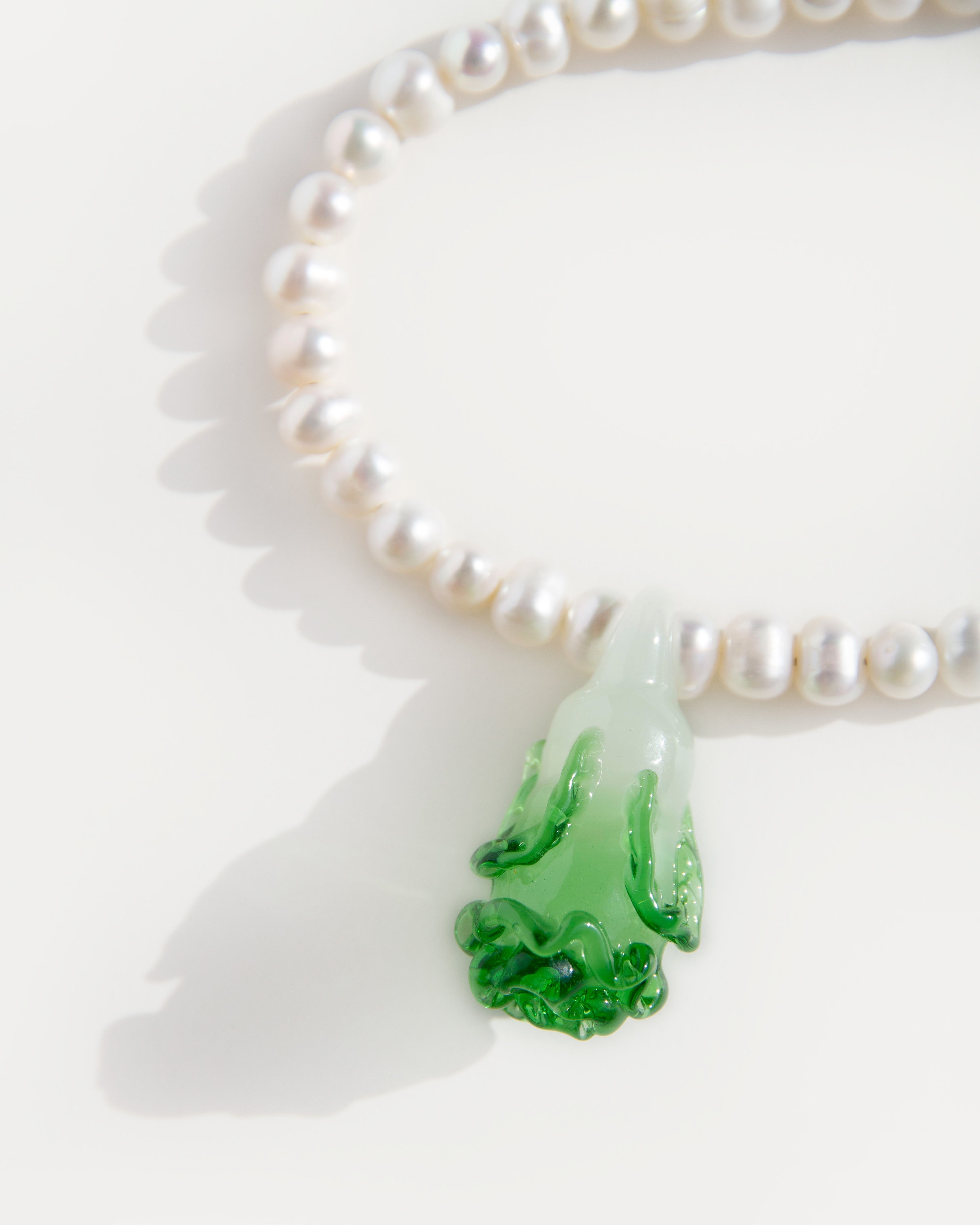 Close-up of green lampwork glass pendant shaped like bok choy on Cabbage Pearl Necklace with natural freshwater pearls and subtle shadows.
