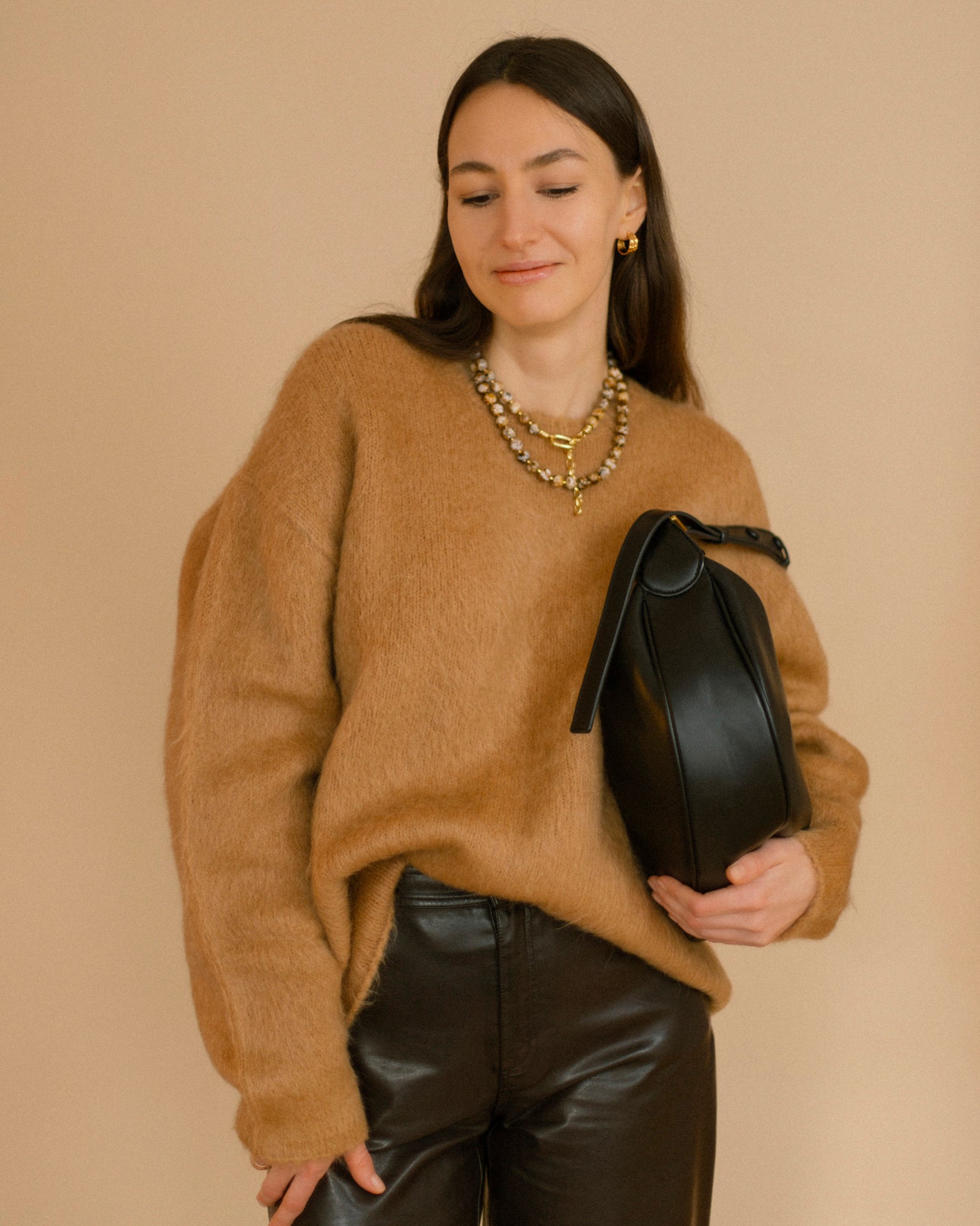 Model in camel sweater and black leather pants wearing the Coffee Caramel Necklace with polished agate beads in caramel, brown and white with gold details.