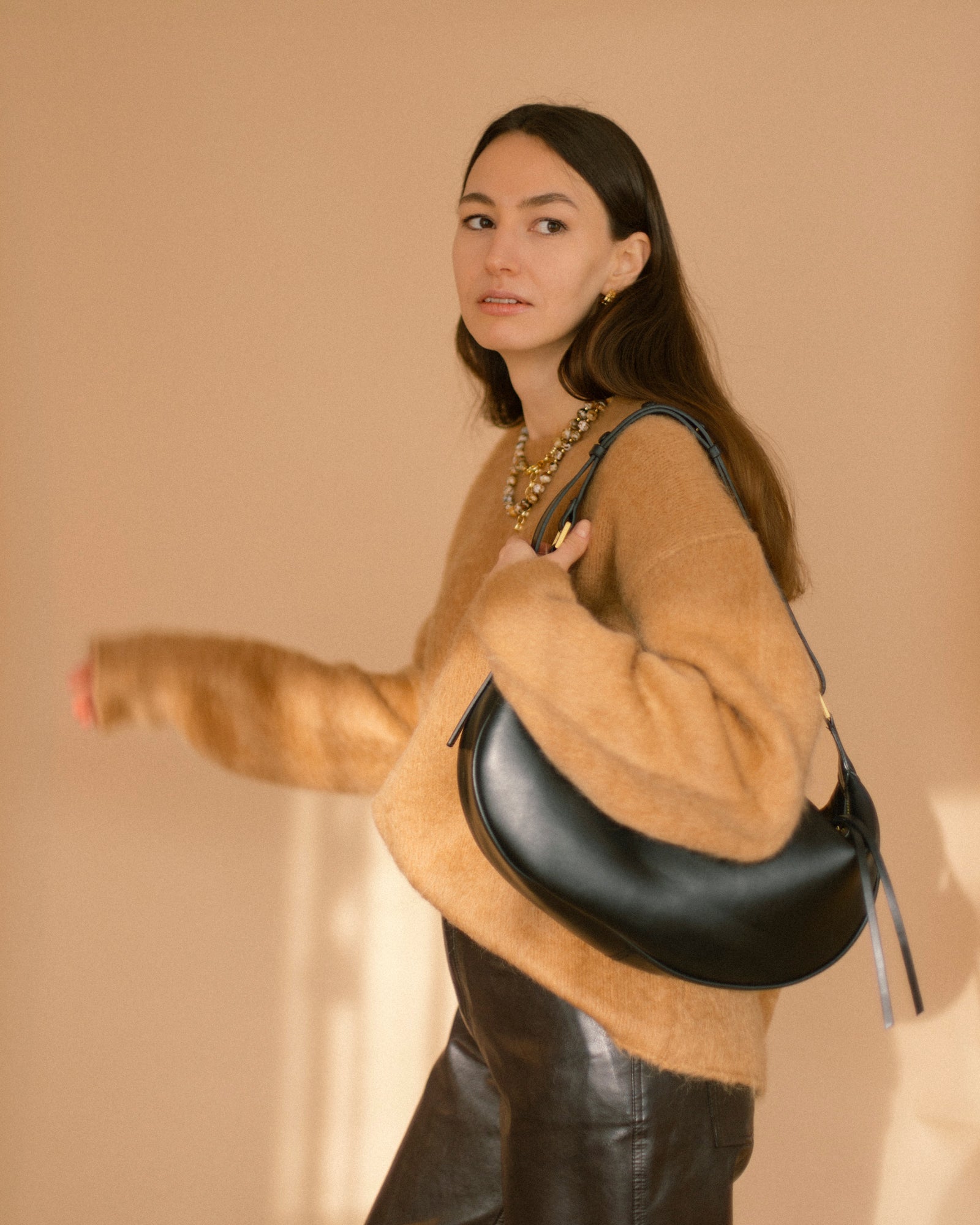 Model in camel sweater and black leather pants carrying a black shoulder bag, styled with the Coffee Caramel Necklace of agate beads in caramel, brown and white.