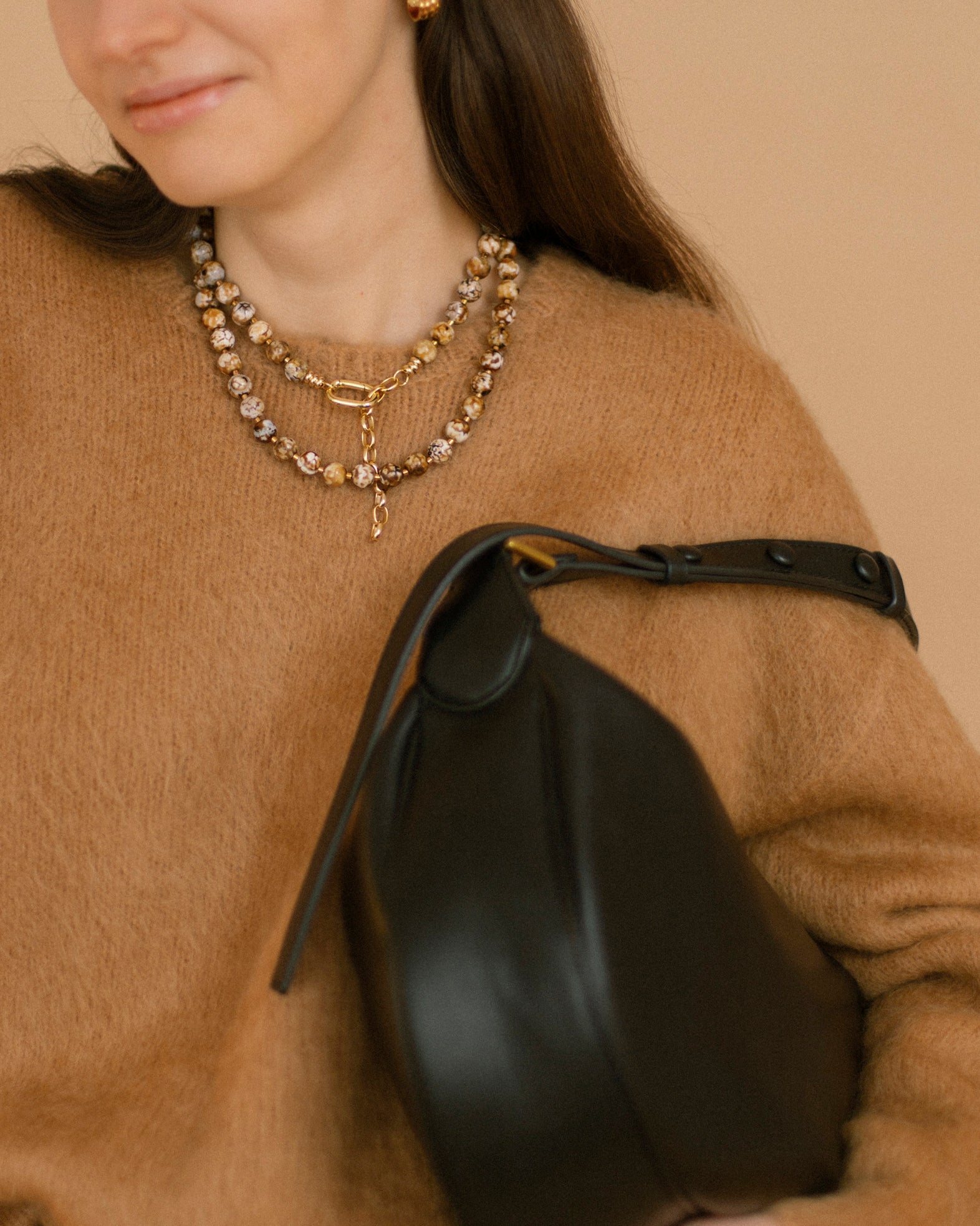 Model wearing the Coffee Caramel Necklace with polished agate beads in caramel, brown and white tones with gold accents, styled over a camel sweater.