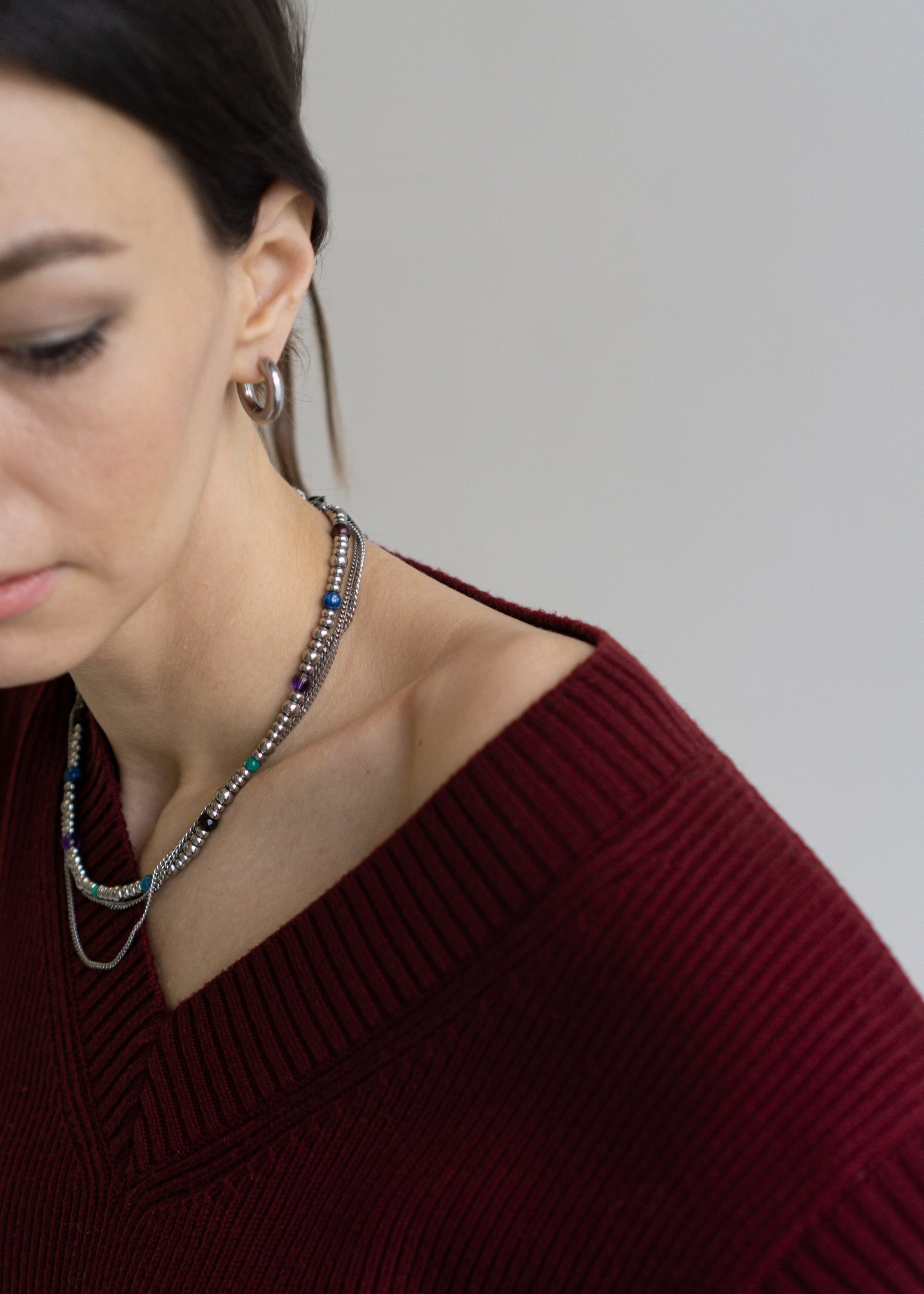 Side profile of a model featuring a clean ear, neck, and shoulder line, accented by a sleek silver hoop earring and the GEMS necklace. The layered design of the necklace, with its colorful natural gemstones and durable stainless steel, adds a subtle yet stylish detail, showcasing its minimalist elegance. Ideal for demonstrating how Jewell Reef's unique jewelry enhances personal style for everyday wear or special events.