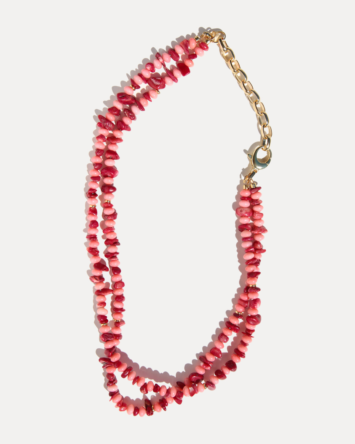 A double-strand pink and deep red coral necklace with a gold chain extender and lobster clasp, shown on a light gray background.