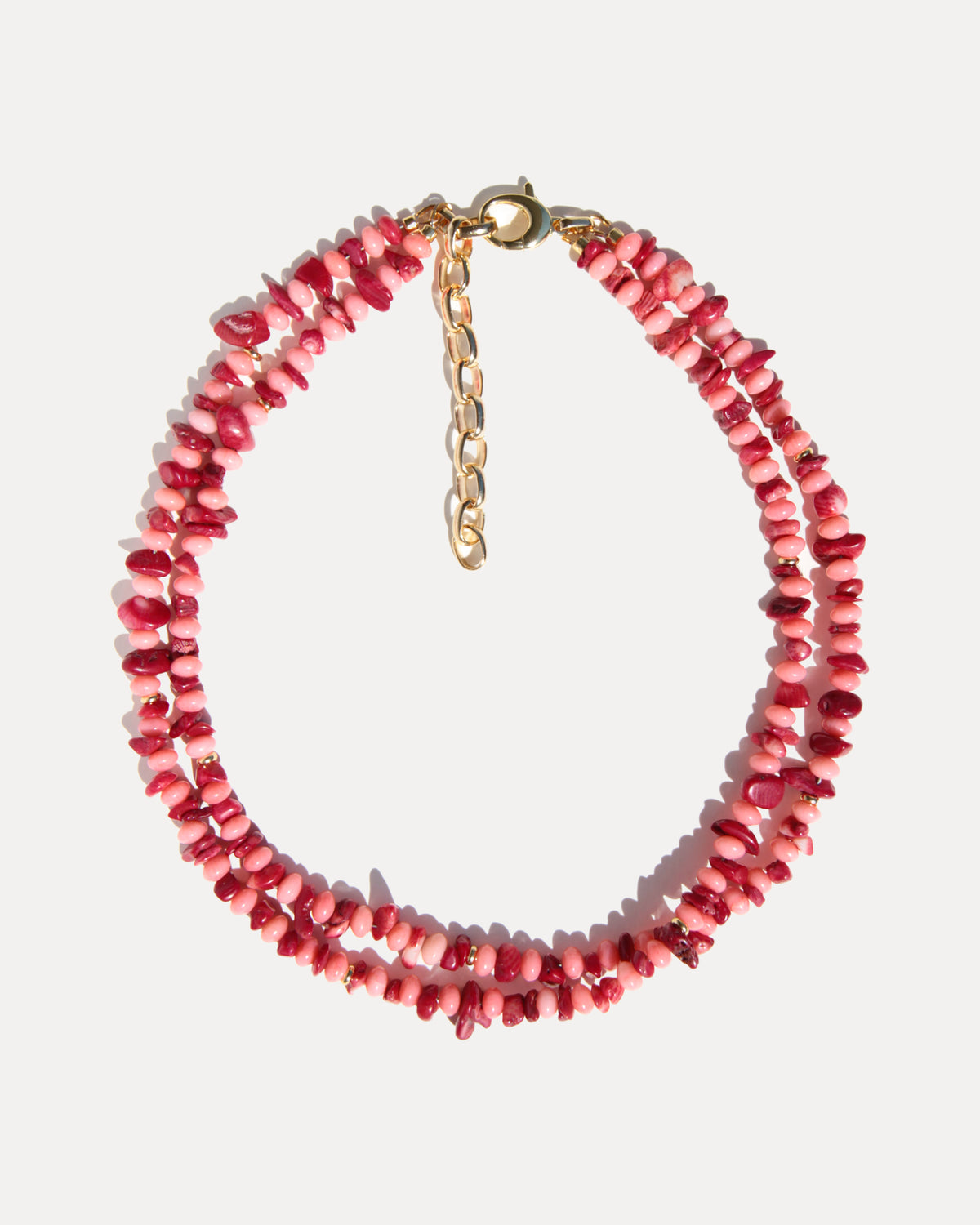 Double-strand pink and deep red coral necklace with gold details on a light background.