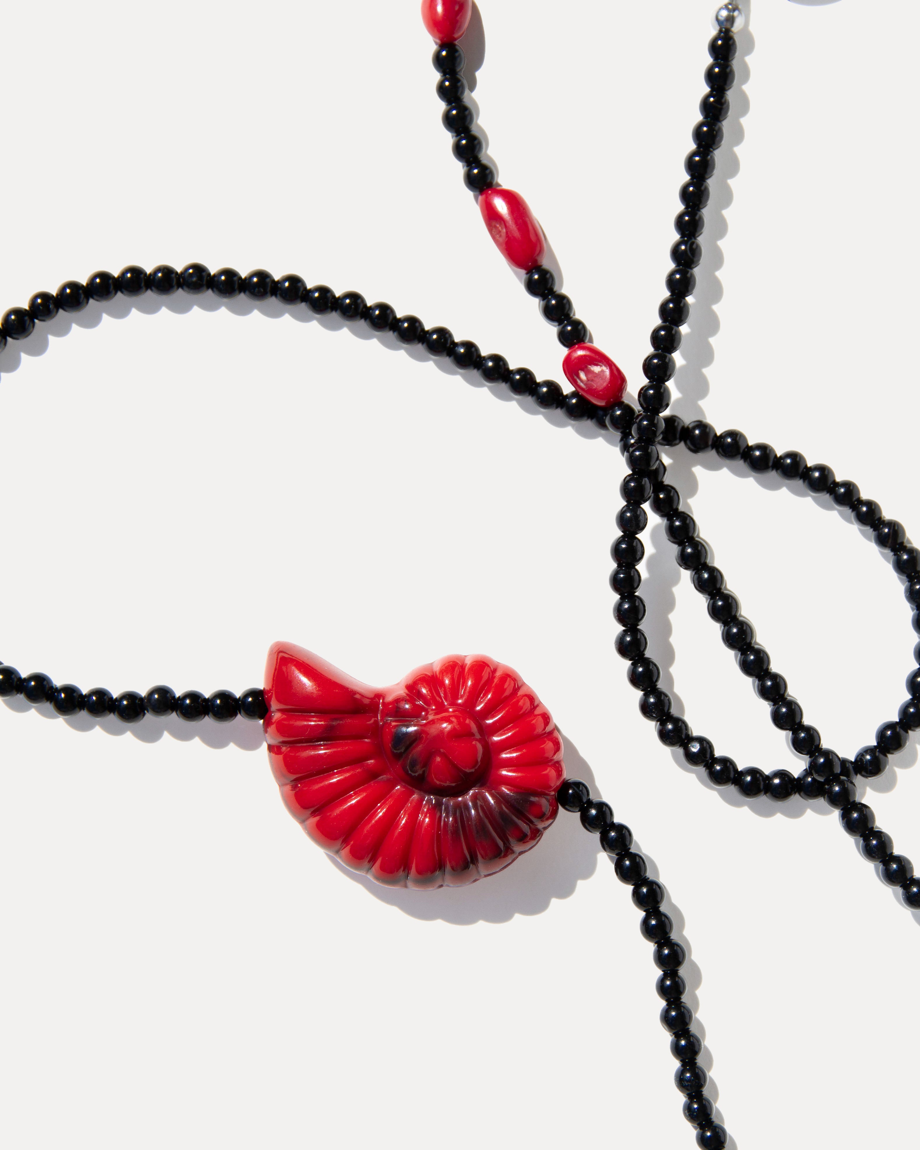 Close-up of a red shell pendant necklace with black agate beads and coral accents