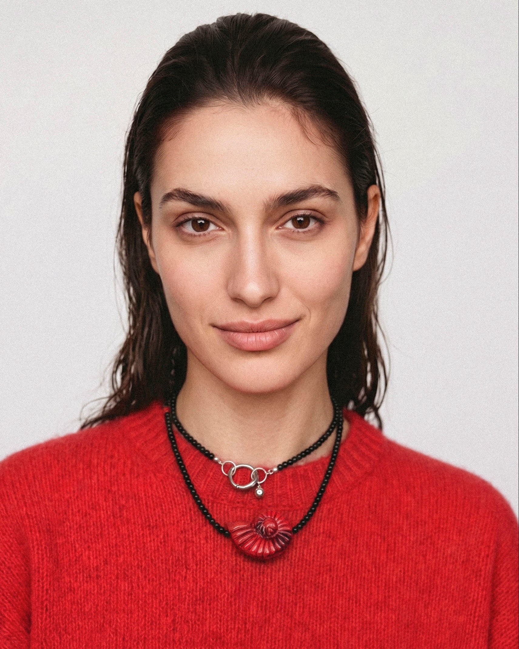 Model wearing a double-layer black agate necklace with a red shell pendant, coral beads and a silver-tone clasp