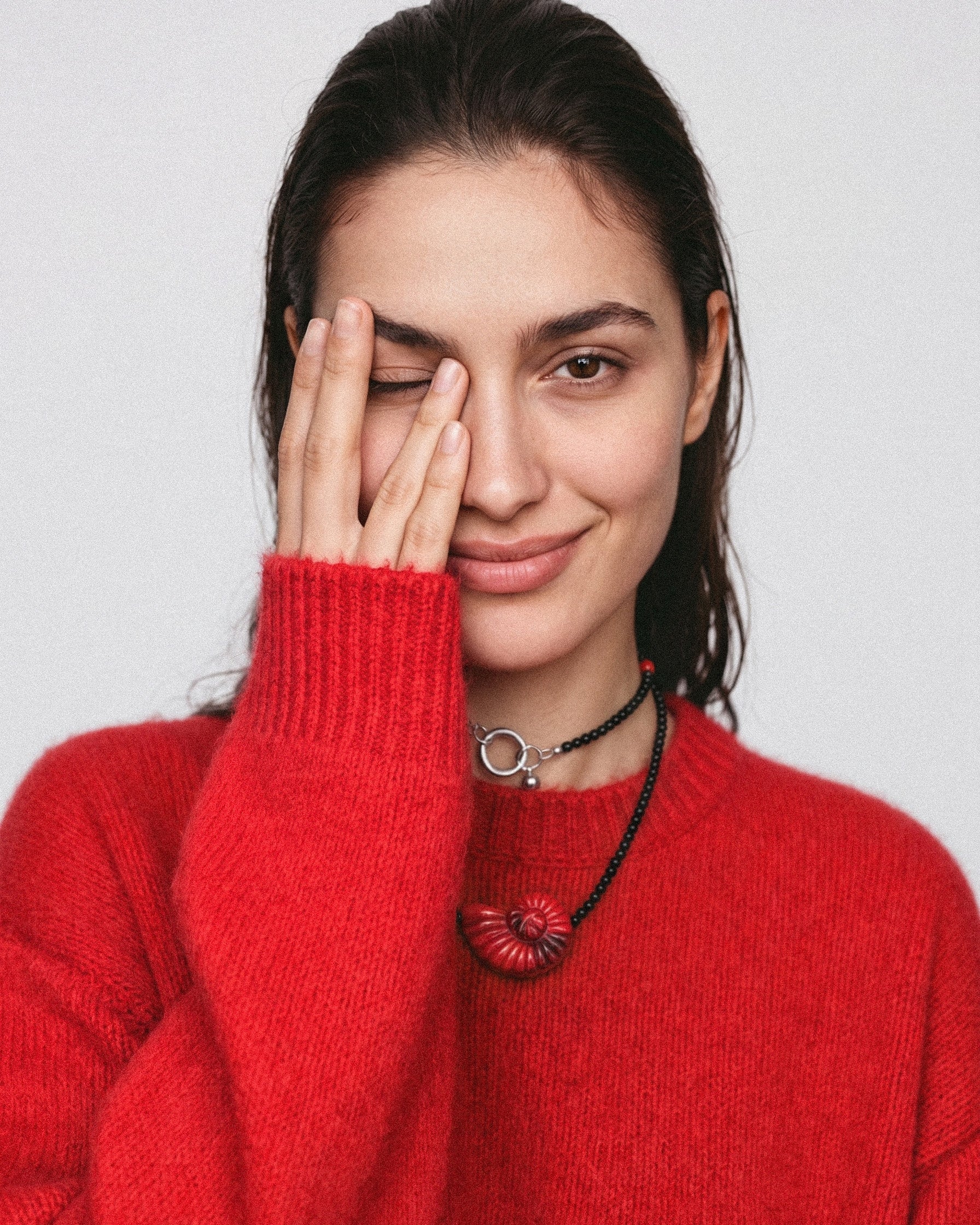 Model wearing a red shell pendant necklace with black agate and coral beads, styled in two layers