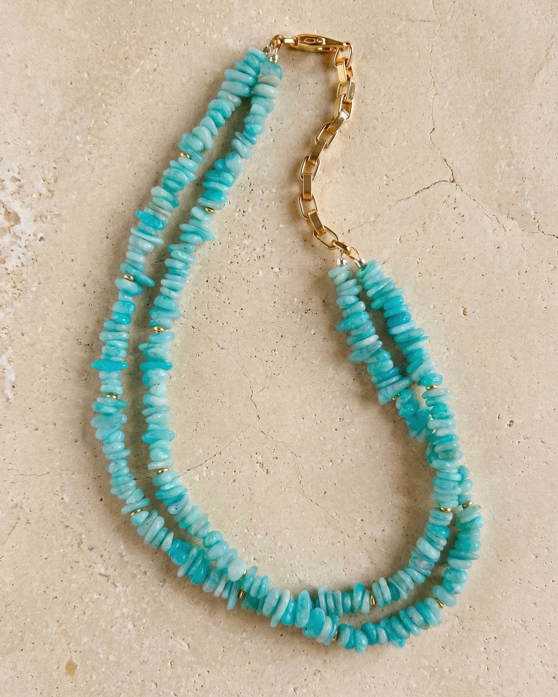 Double strand amazonite necklace with turquoise beads and gold-plated clasp photographed on a textured natural stone surface.