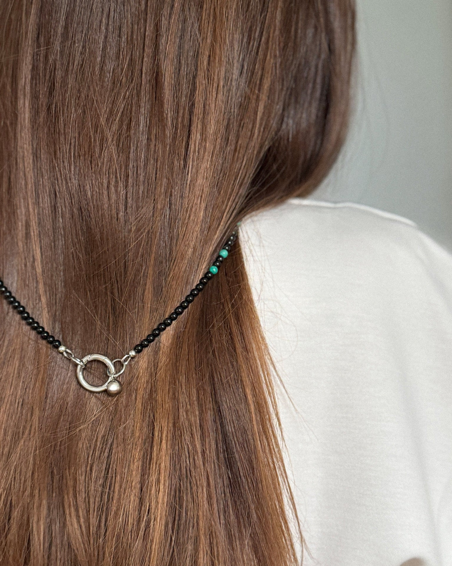 Close-up of Emerald Shell Necklace clasp, showing stainless steel ring closure with glossy black agate beads and subtle amazonite accents.