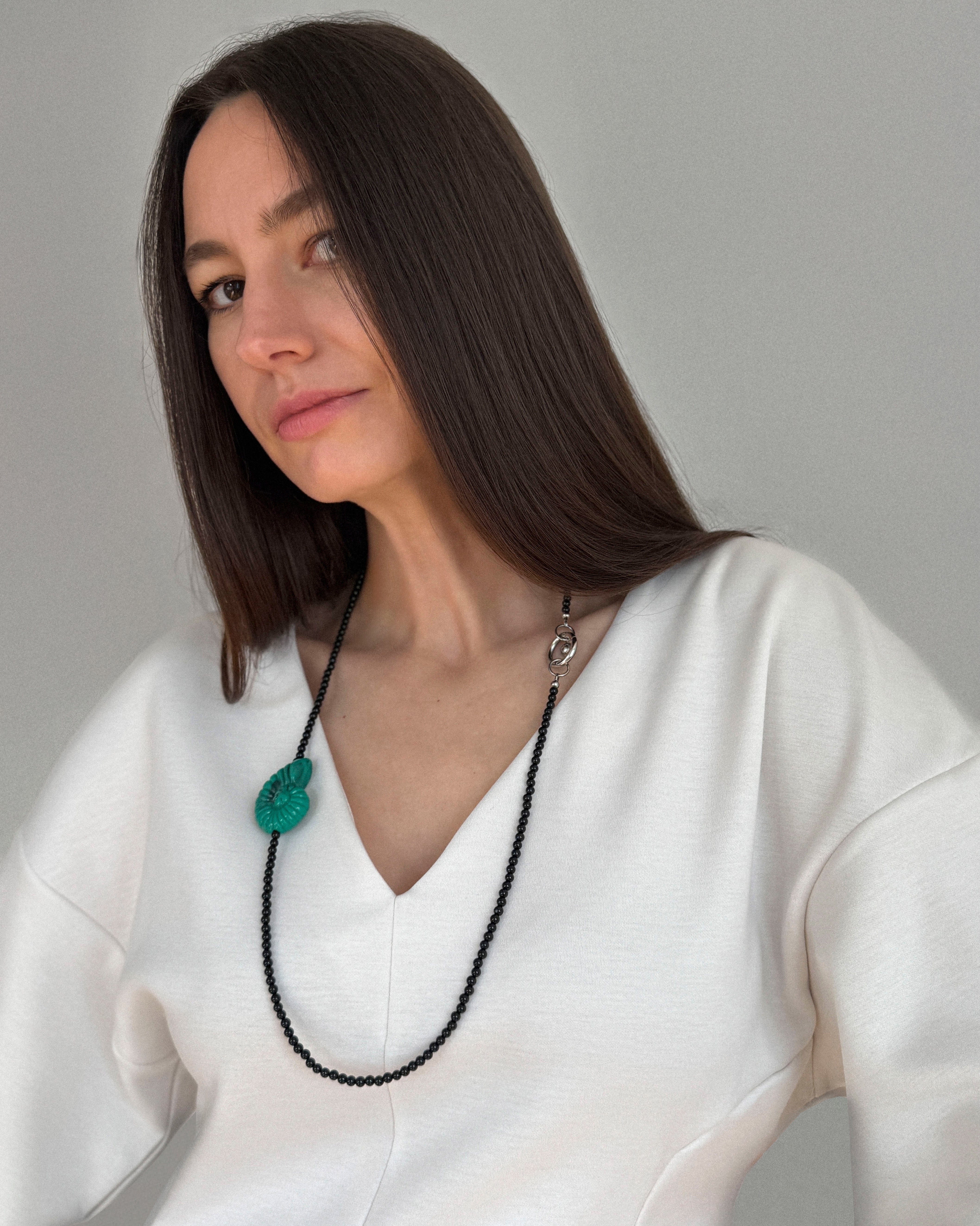 Model wearing Emerald Shell Necklace with glossy black agate beads and emerald-green shell pendant, styled over a white V-neck blouse.