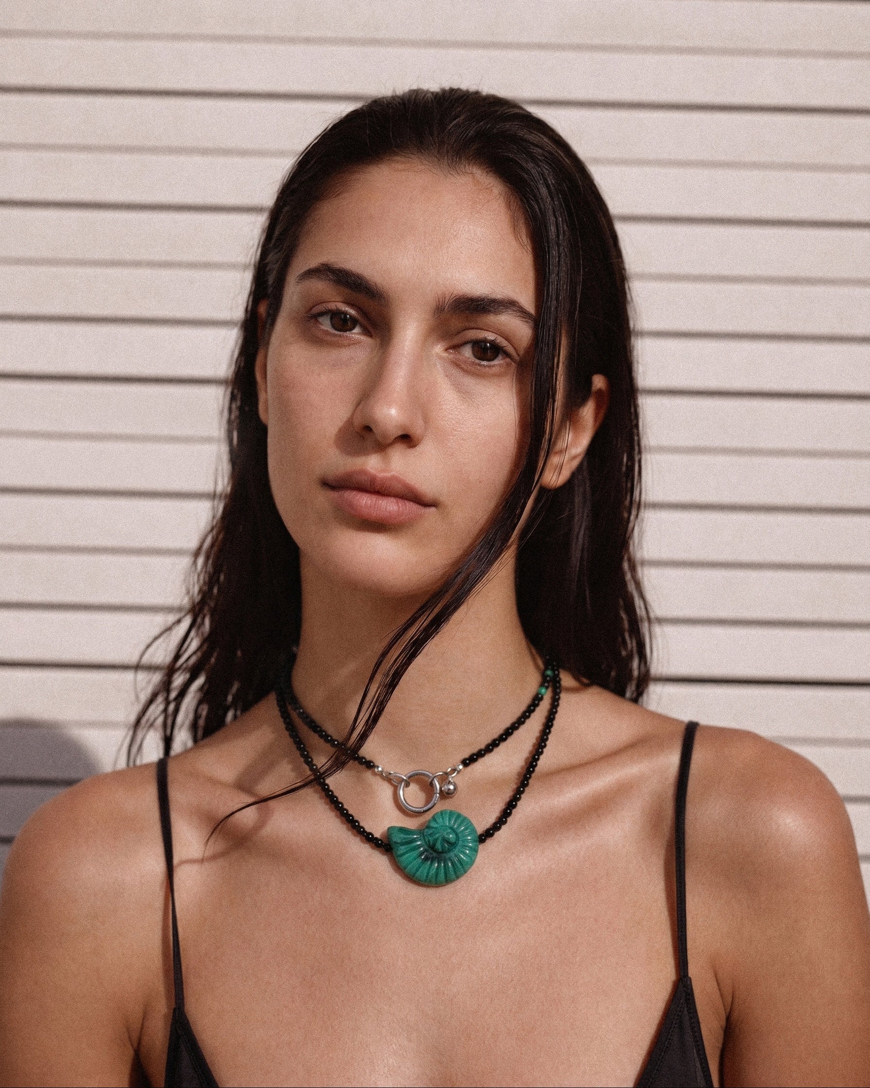 Model wearing a long black agate necklace with an emerald green shell bead, styled doubled around the neck with a black slip dress.