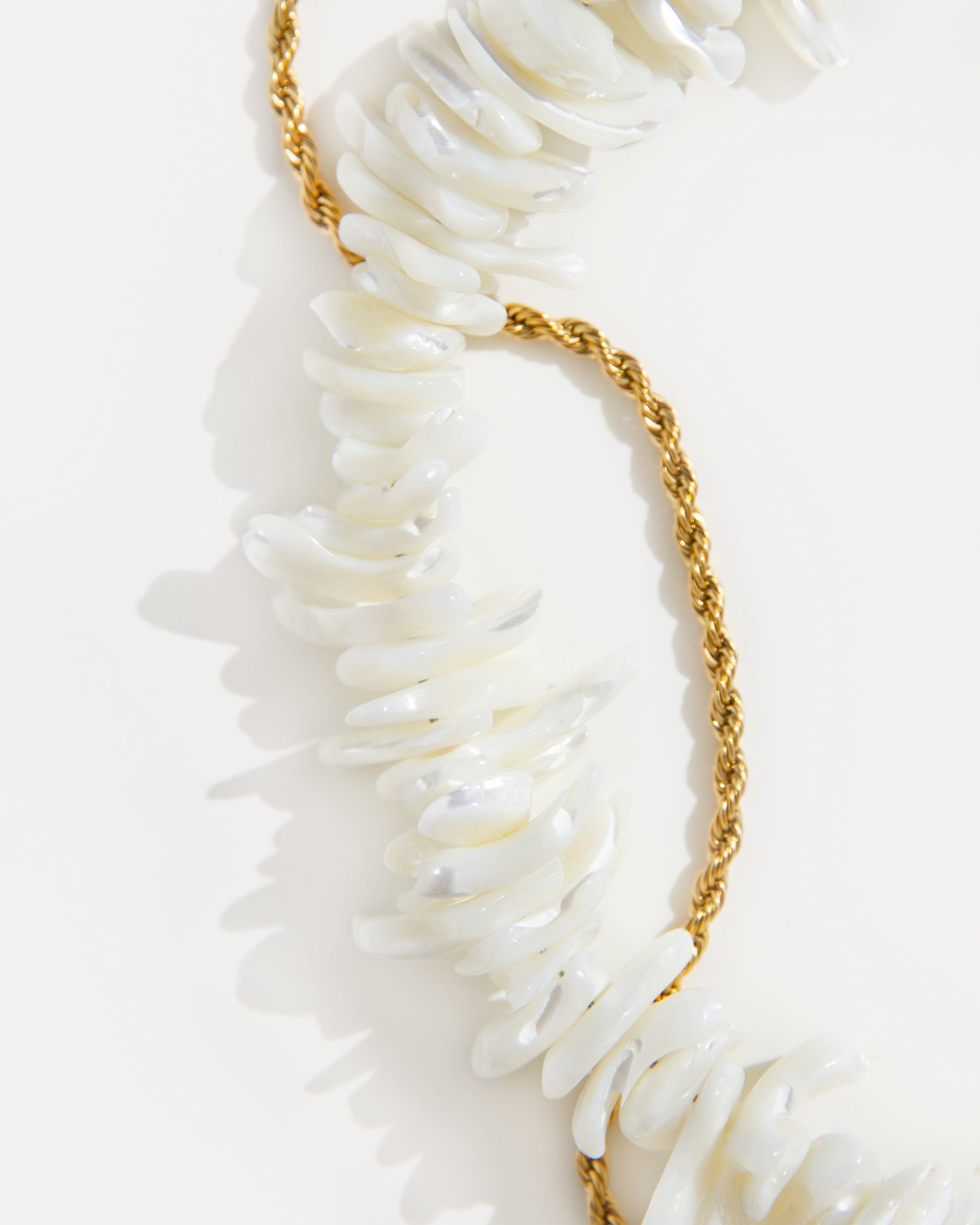 close-up of statement shell choker necklace with iridescent shell beads and twisted 18K gold-plated chain on white background