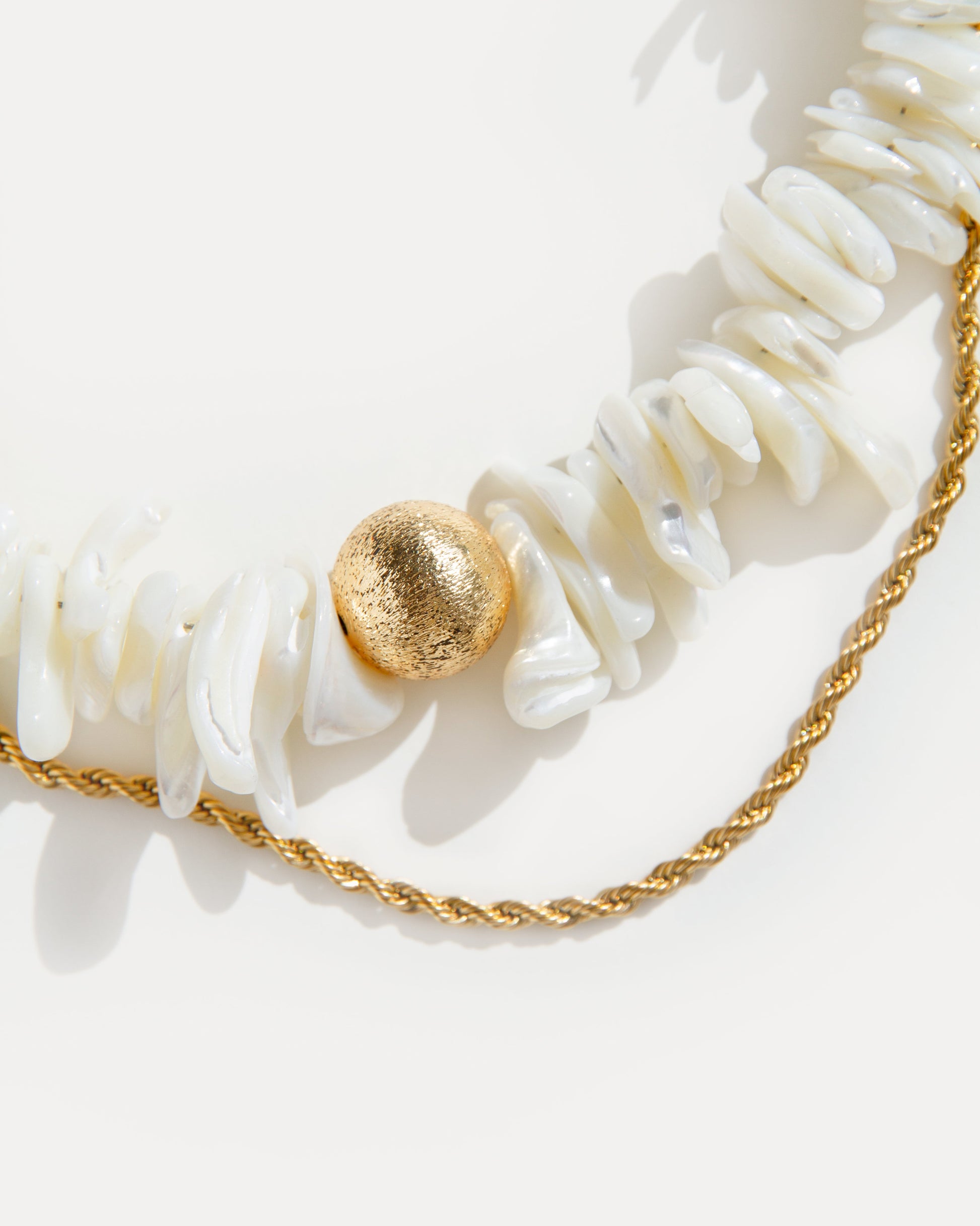 close-up of statement shell choker necklace with white shell beads, textured gold detail and twisted gold-plated chain