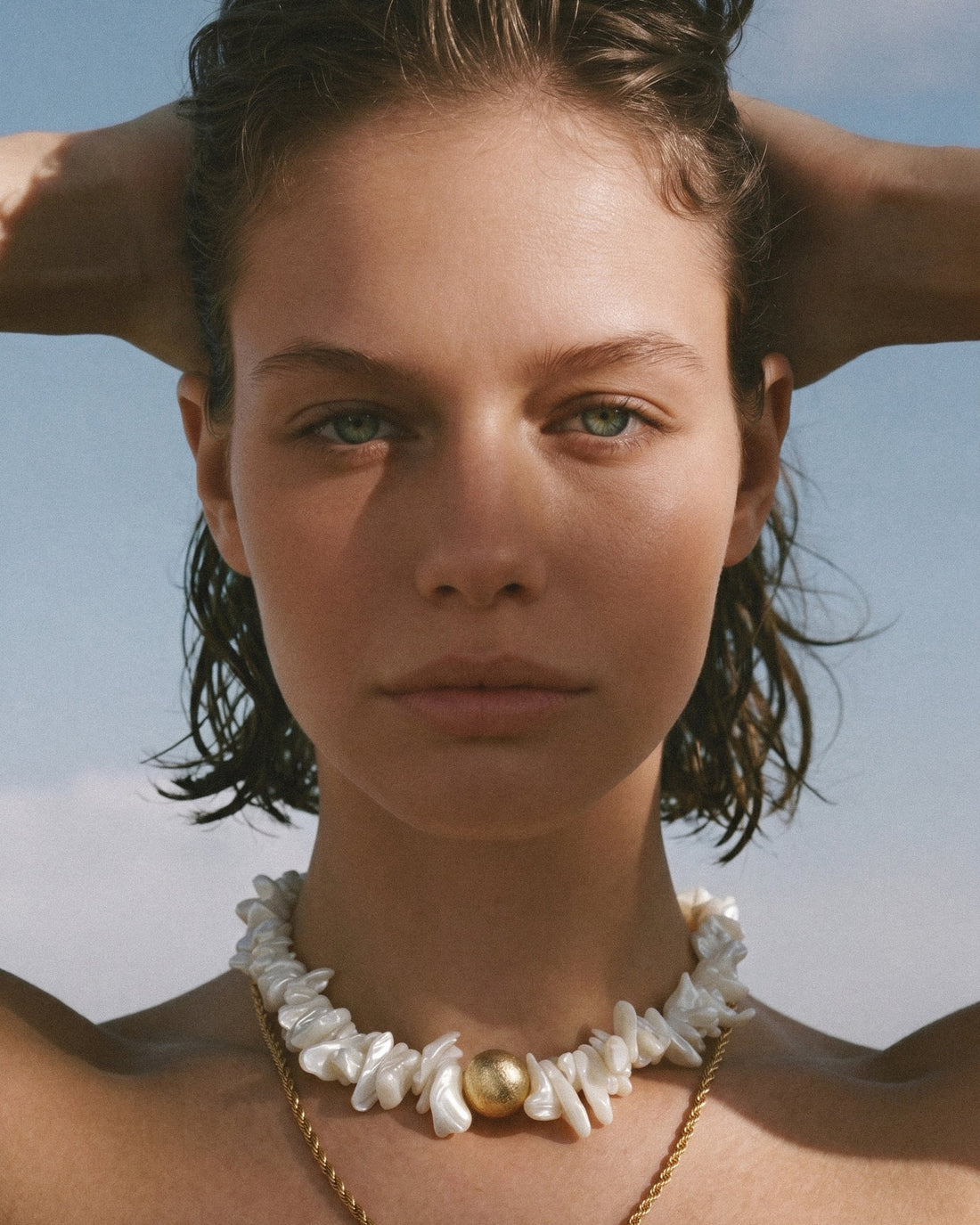 statement shell choker necklace with white shell beads and twisted 18K gold-plated chain arranged on white background