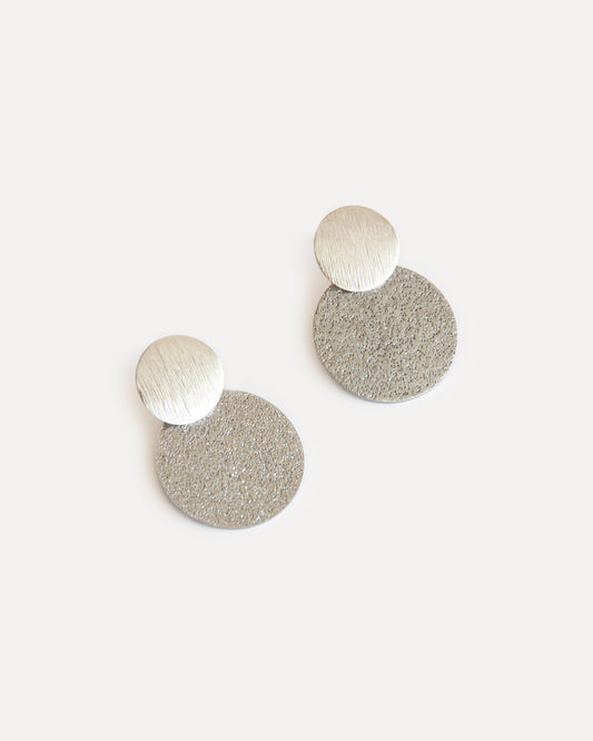 Minimalist silver statement earrings with two textured discs in contrasting finishes, crafted from stainless steel for a modern, sculptural look.