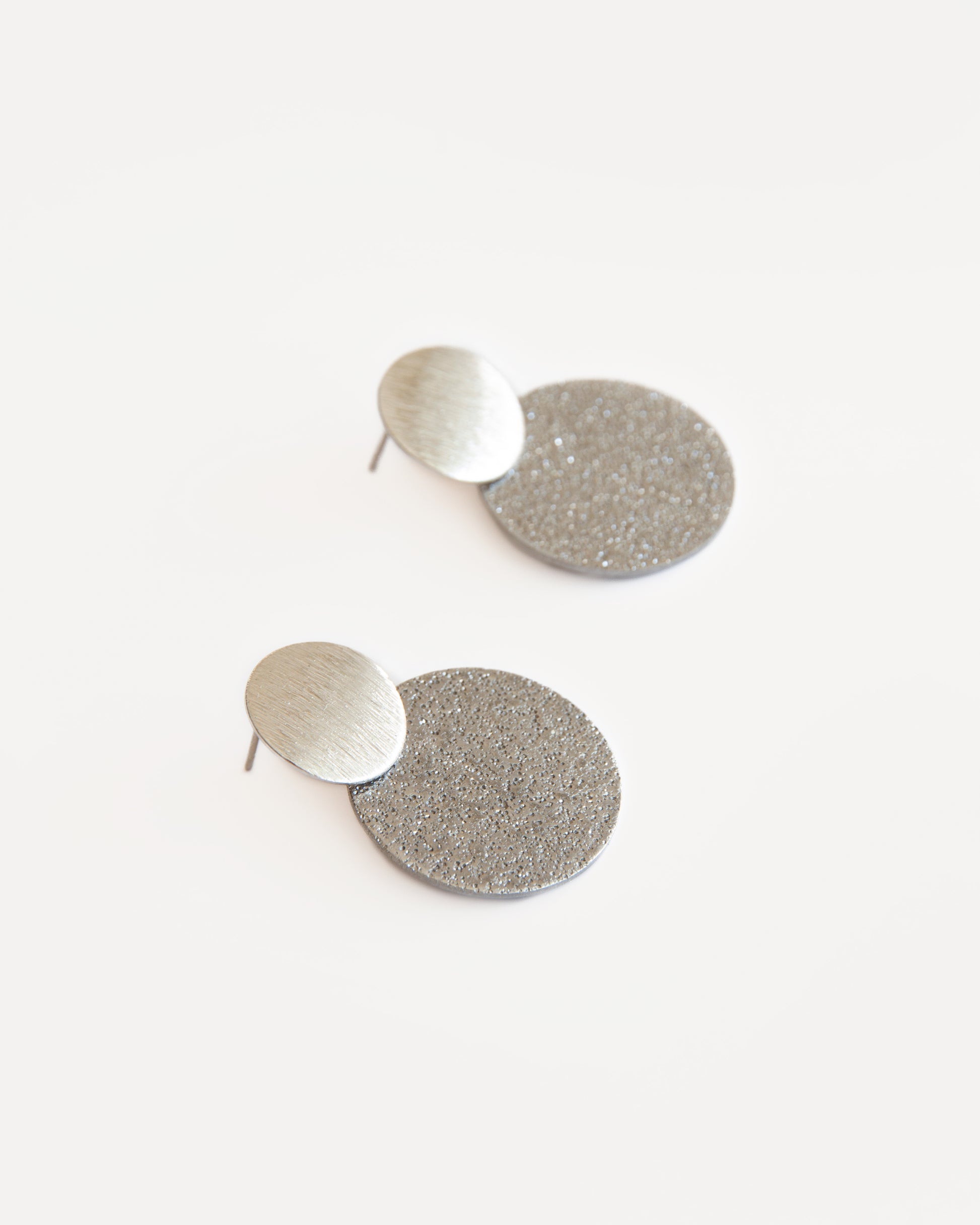 Fly Me to the Moon Earrings — silver double-disc statement studs with matte and textured finish, creating a minimalist geometric look with modern elegance.