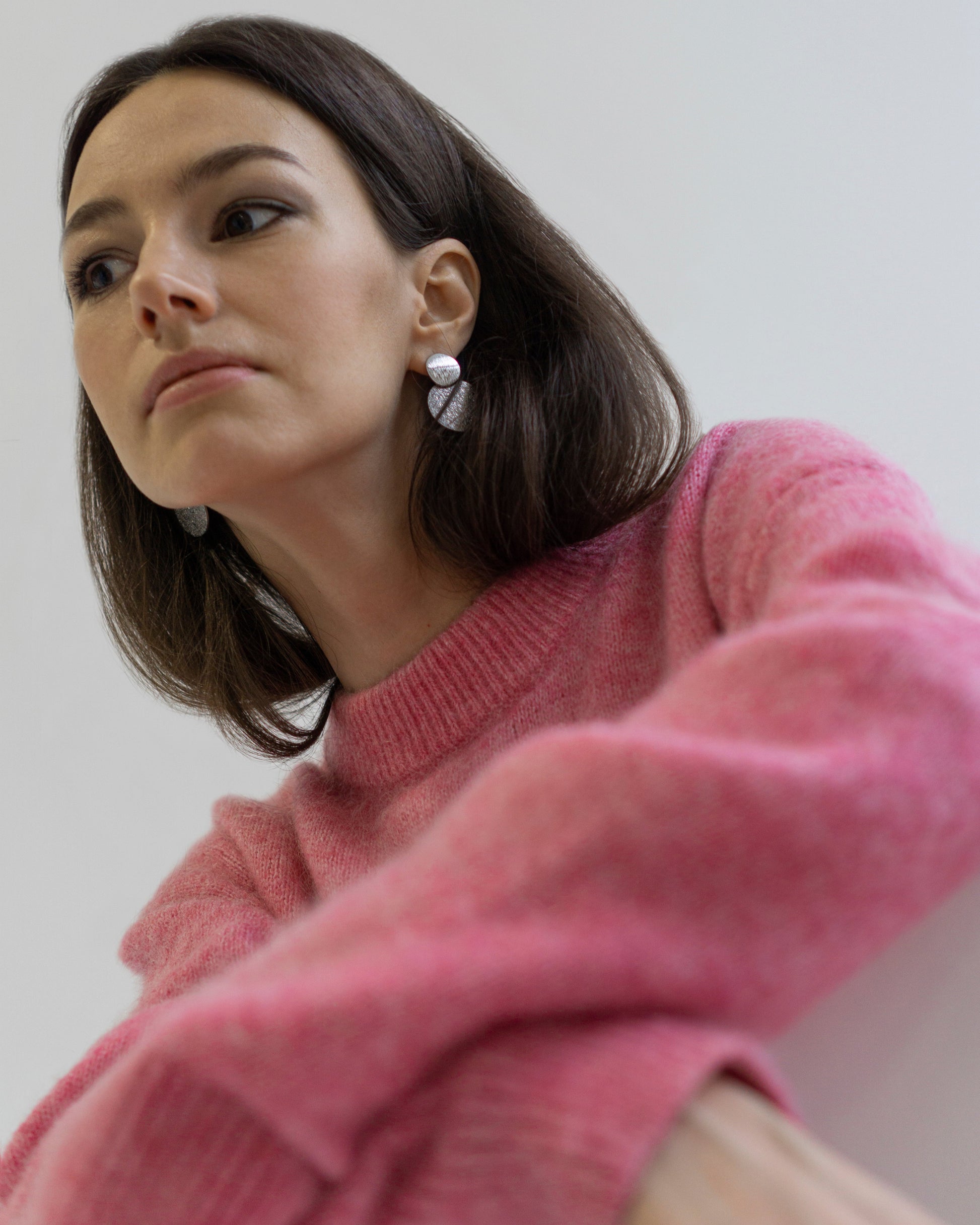 Model wearing Fly Me to the Moon silver statement earrings with pink sweater. Geometric double-disc design adds modern elegance to a casual chic look.