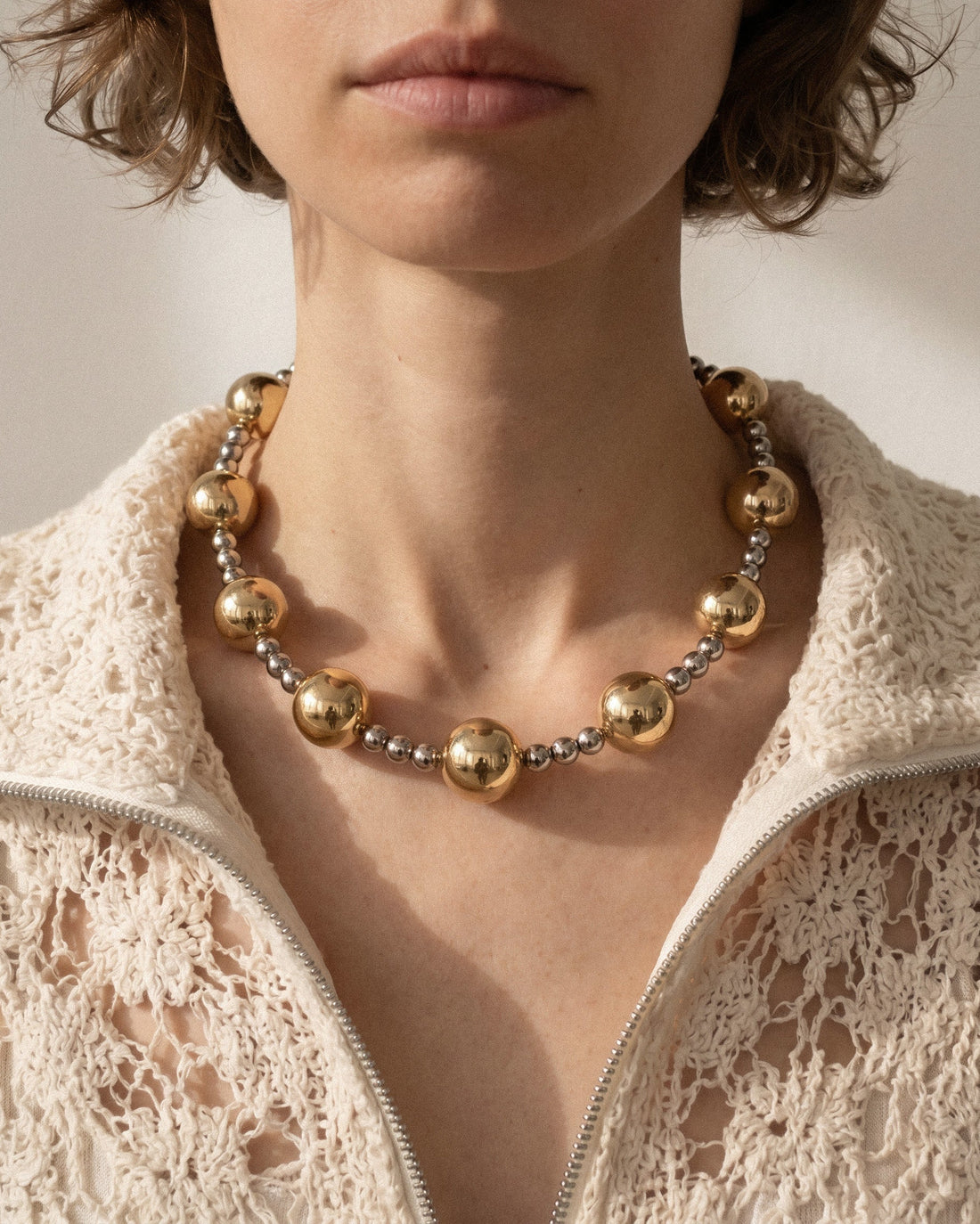mixed metal beaded necklace with gold and silver beads arranged in a clean circular shape on white background