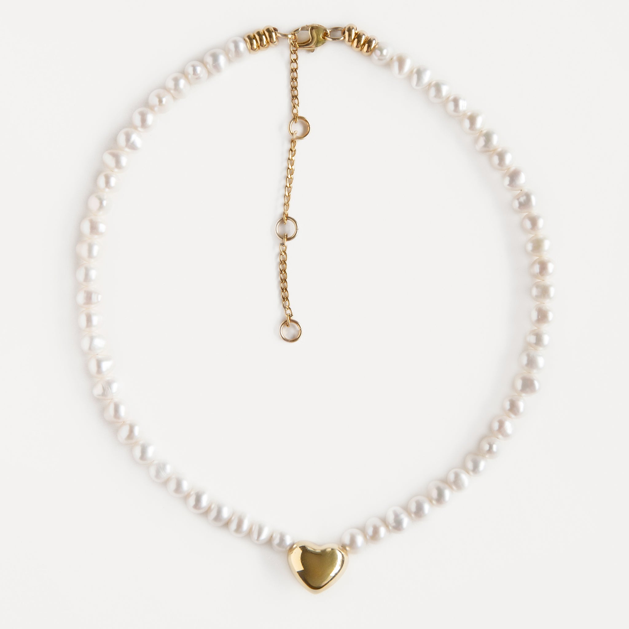 Delicate pearl choker with an 18K gold-plated heart pendant and adjustable chain. Elegant modern necklace that adds warmth and soft shine to any look.