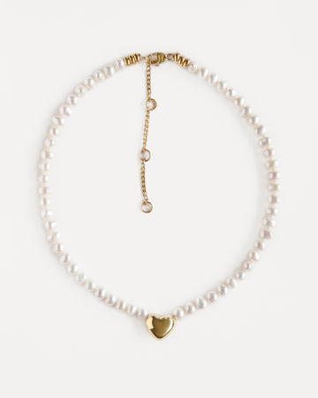 Delicate pearl choker with an 18K gold-plated heart pendant and adjustable chain. Elegant modern necklace that adds warmth and soft shine to any look.