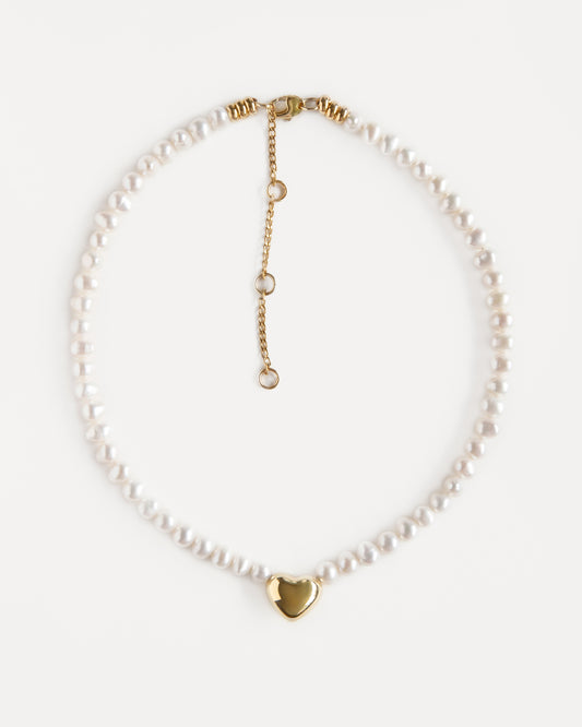 Delicate pearl choker with an 18K gold-plated heart pendant and adjustable chain. Elegant modern necklace that adds warmth and soft shine to any look.