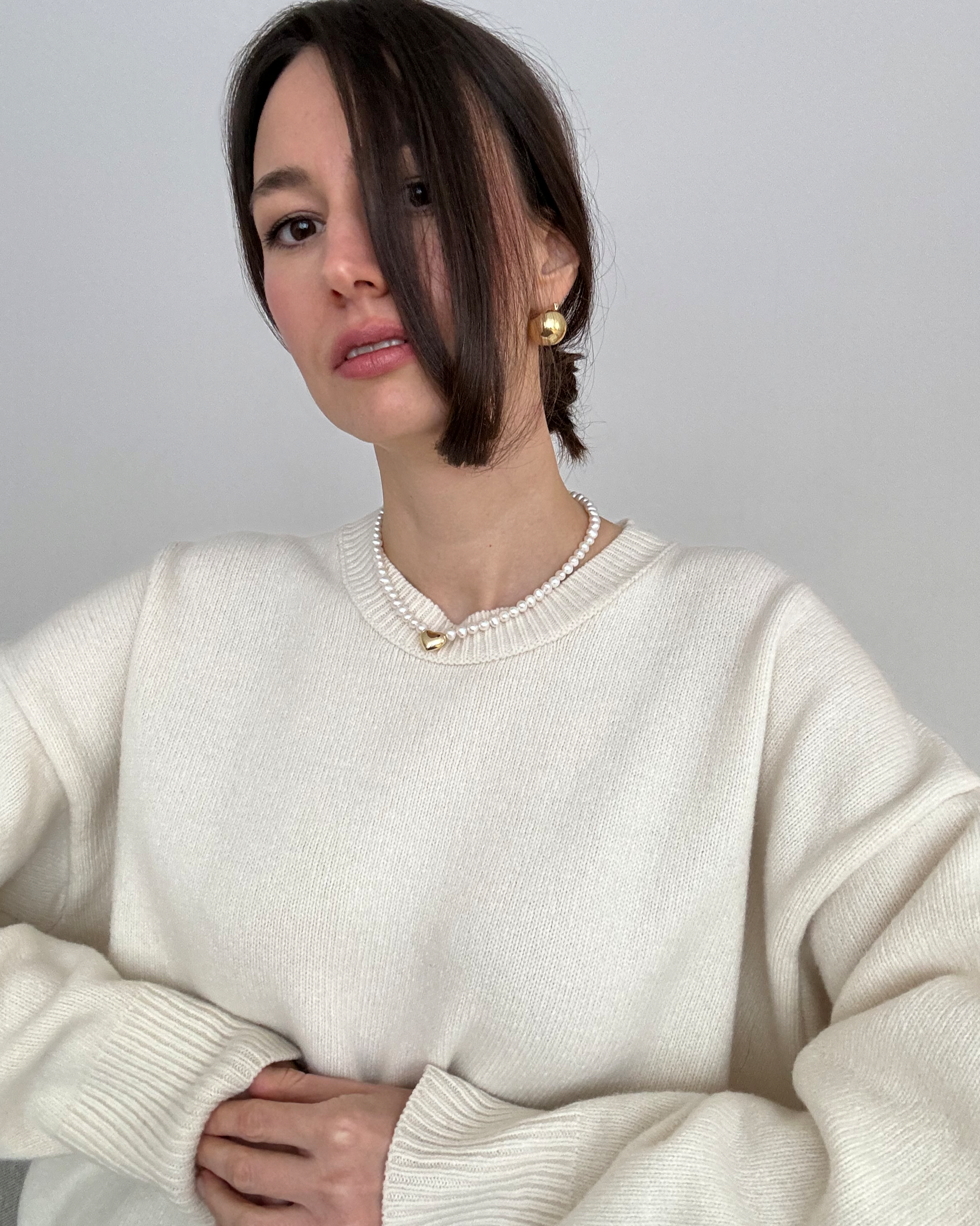 Model wearing the Heart of Gold Necklace — a pearl choker with an 18K gold-plated heart charm. A refined, timeless piece that adds warmth to minimal looks.