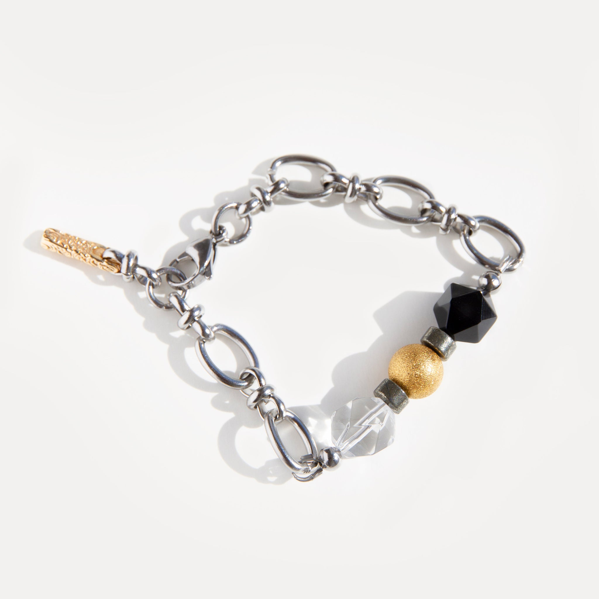 The Jazz Bracelet, laid flat and gently curved, highlighting its unique design of natural clear quartz, deep black agate, and golden 18K gold-plated brass beads, all set on a robust stainless steel chain with secure lobster clasp. This bold yet refined mixed-metal bracelet offers a versatile minimalist statement, perfect for everyday wear or creative layering. Discover Jewell Reef's unique handcrafted jewelry for women.