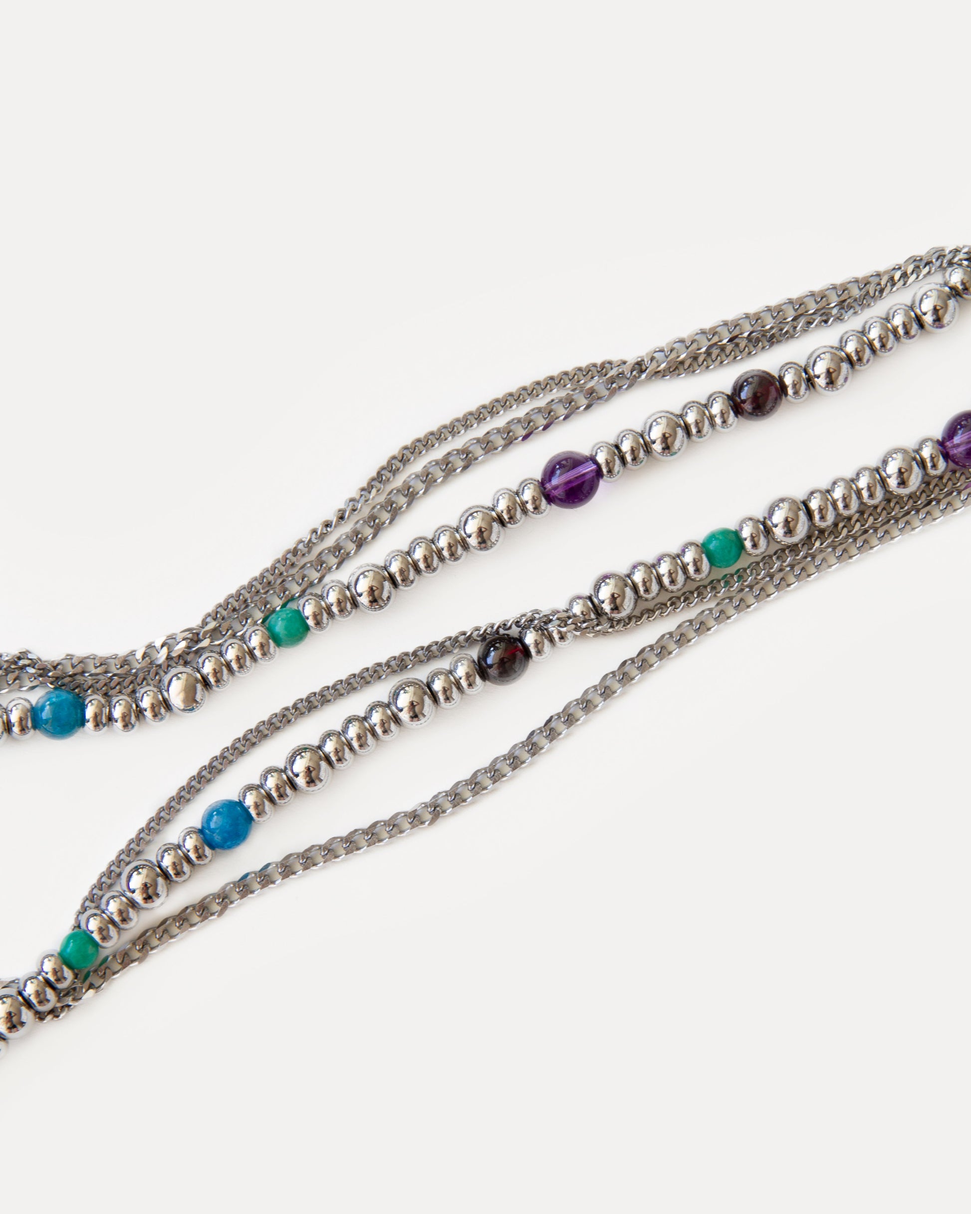 Close-up of the GEMS necklace, a three-layer design showcasing vibrant natural gemstones including amethyst, kyanite, and turquoise-toned apatite beads, interspersed with shiny jewelry steel spheres and delicate chains. This detailed shot highlights the modern, minimalist yet playful aesthetic, perfect for everyday style or special occasion layering. Discover unique, handcrafted jewelry by Jewell Reef, ideal for versatile statement pieces and thoughtful gifts.