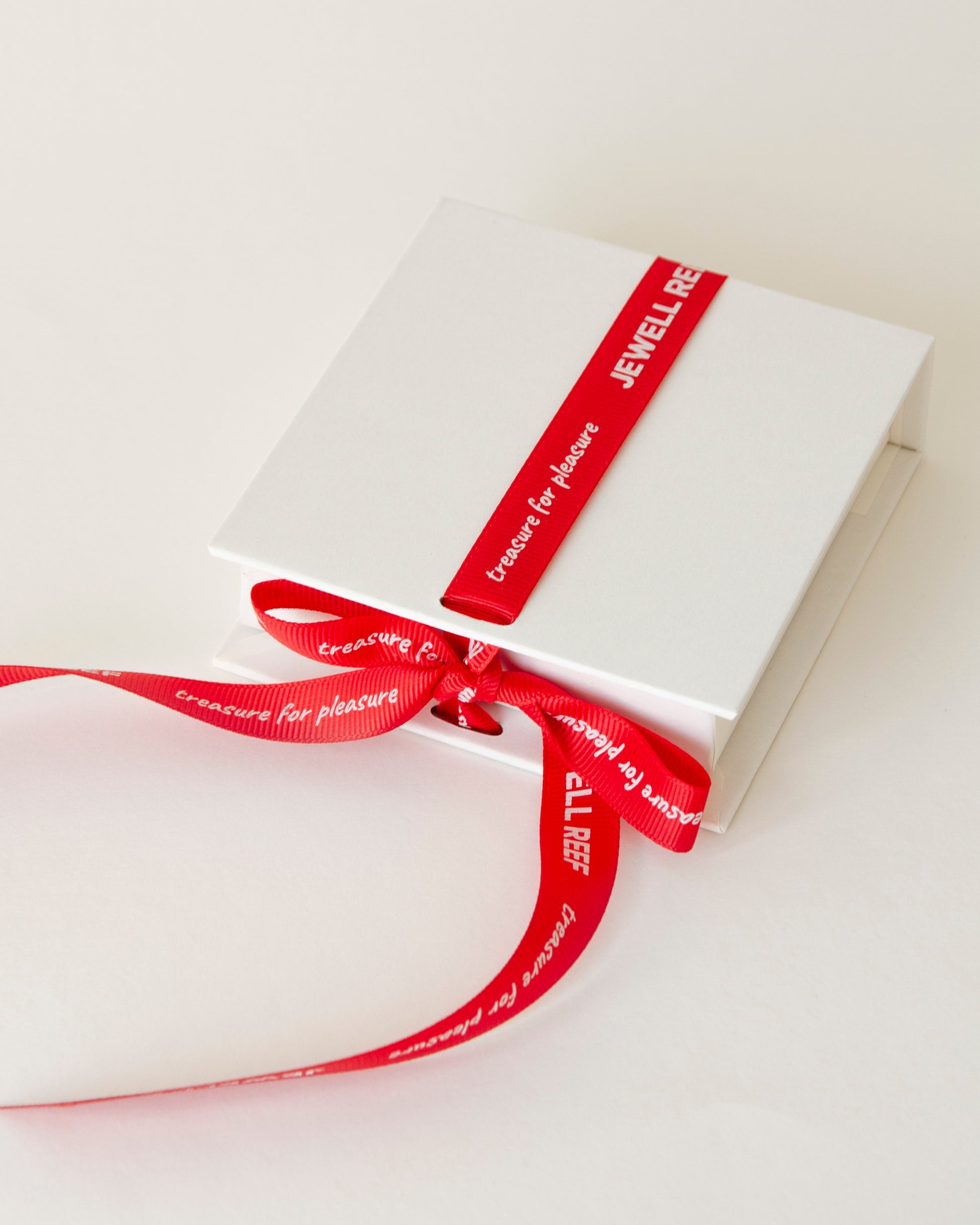 Elegant white jewelry box tied with a red ribbon featuring the "Jewell Reef" logo. 