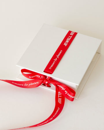 Elegant white jewelry box tied with a red ribbon featuring the "Jewell Reef" logo. 