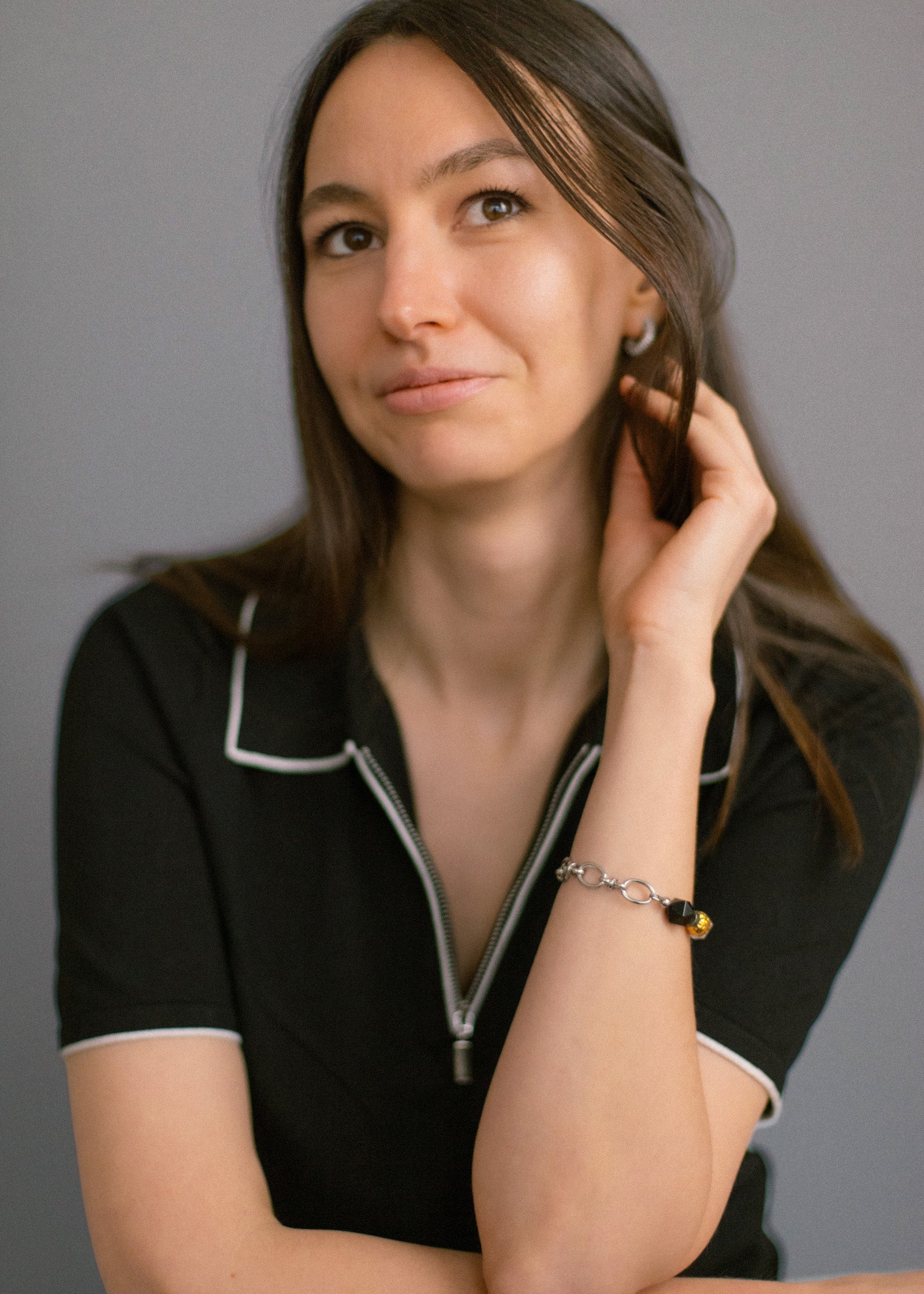 Smiling woman in a black collared shirt, elegantly showcasing the Jazz Bracelet on her wrist. This close-up highlights the bracelet's unique mix of natural clear quartz, deep agate, and gold-plated brass beads on a durable stainless steel chain. A bold yet refined minimalist accessory by Jewell Reef, perfect for adding confidence and style to everyday looks. Explore unique handcrafted jewelry gifts