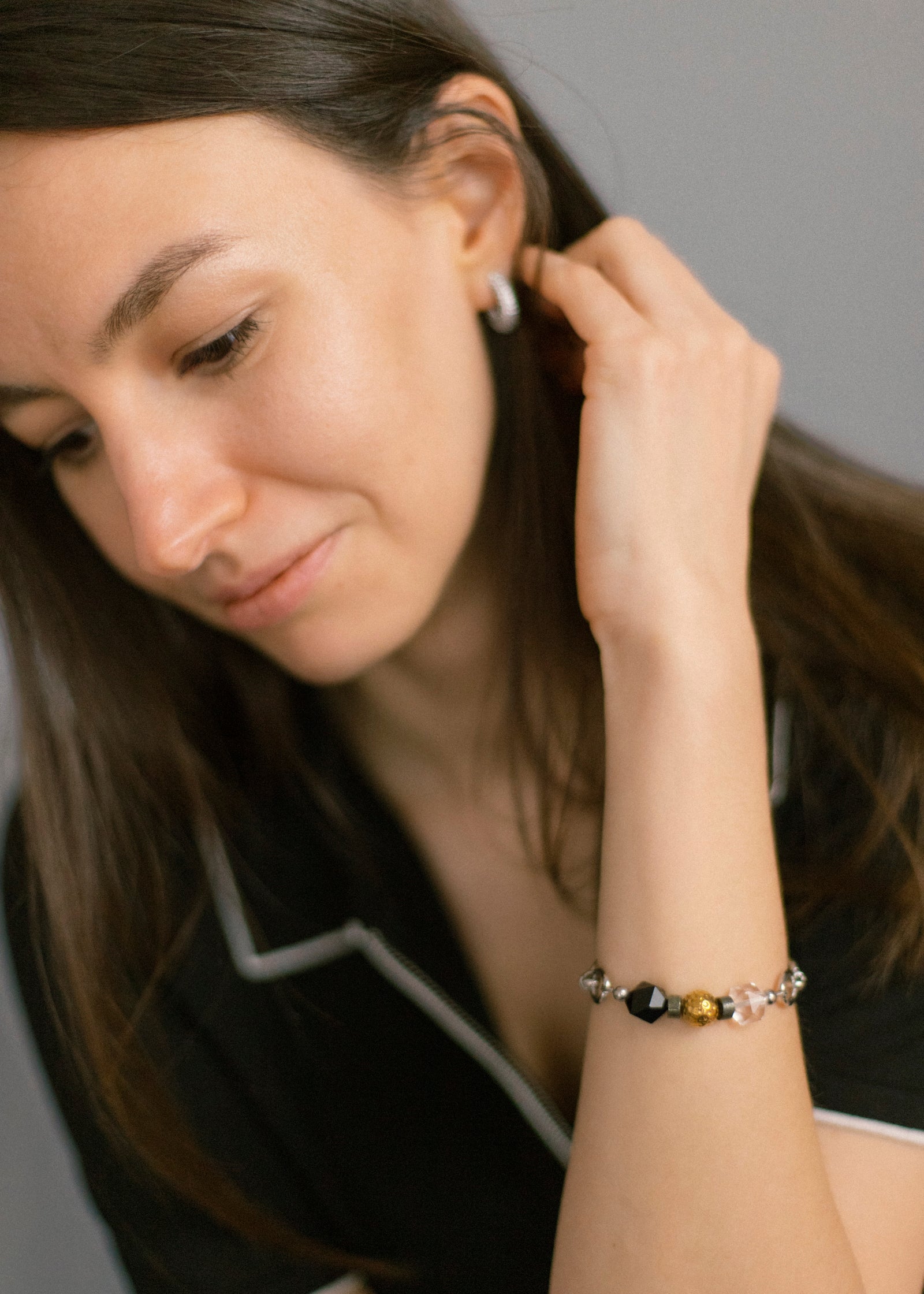 Close-up of a woman's arm, with her hand gently touching her hair, showcasing the Jazz Bracelet on her wrist. The bracelet features natural clear quartz, deep black agate, and golden 18K gold-plated brass beads on a sleek stainless steel chain. This image highlights the comfortable fit and versatile minimalist style of Jewell Reef's unique handmade jewelry for everyday wear and quiet confidence.
