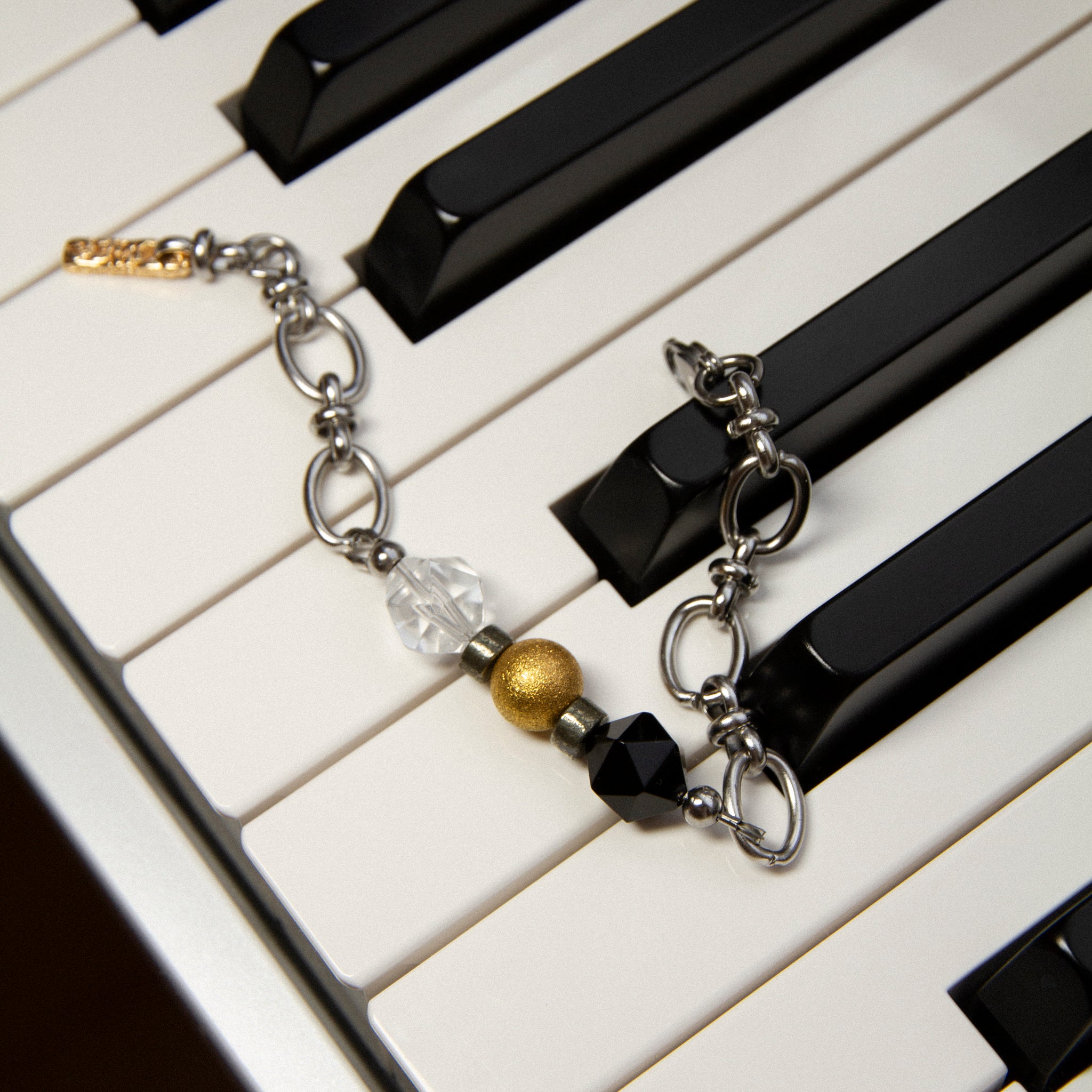The Jazz Bracelet artistically displayed on black and white piano keys, visually connecting to its musical inspiration of rhythm and harmony. This unique shot highlights the bracelet's contrast of clear quartz, black agate, and 18K gold-plated brass beads on a sleek stainless steel chain. A bold yet refined minimalist statement piece by Jewell Reef for those who appreciate unique handcrafted jewelry.