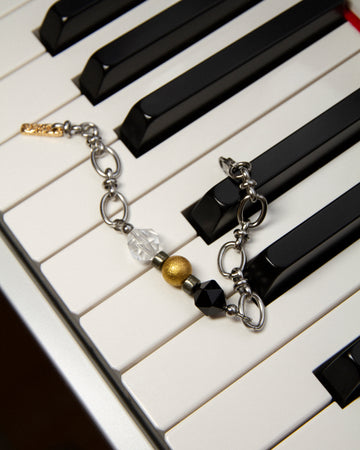 The Jazz Bracelet artistically displayed on black and white piano keys, visually connecting to its musical inspiration of rhythm and harmony. This unique shot highlights the bracelet's contrast of clear quartz, black agate, and 18K gold-plated brass beads on a sleek stainless steel chain. A bold yet refined minimalist statement piece by Jewell Reef for those who appreciate unique handcrafted jewelry.