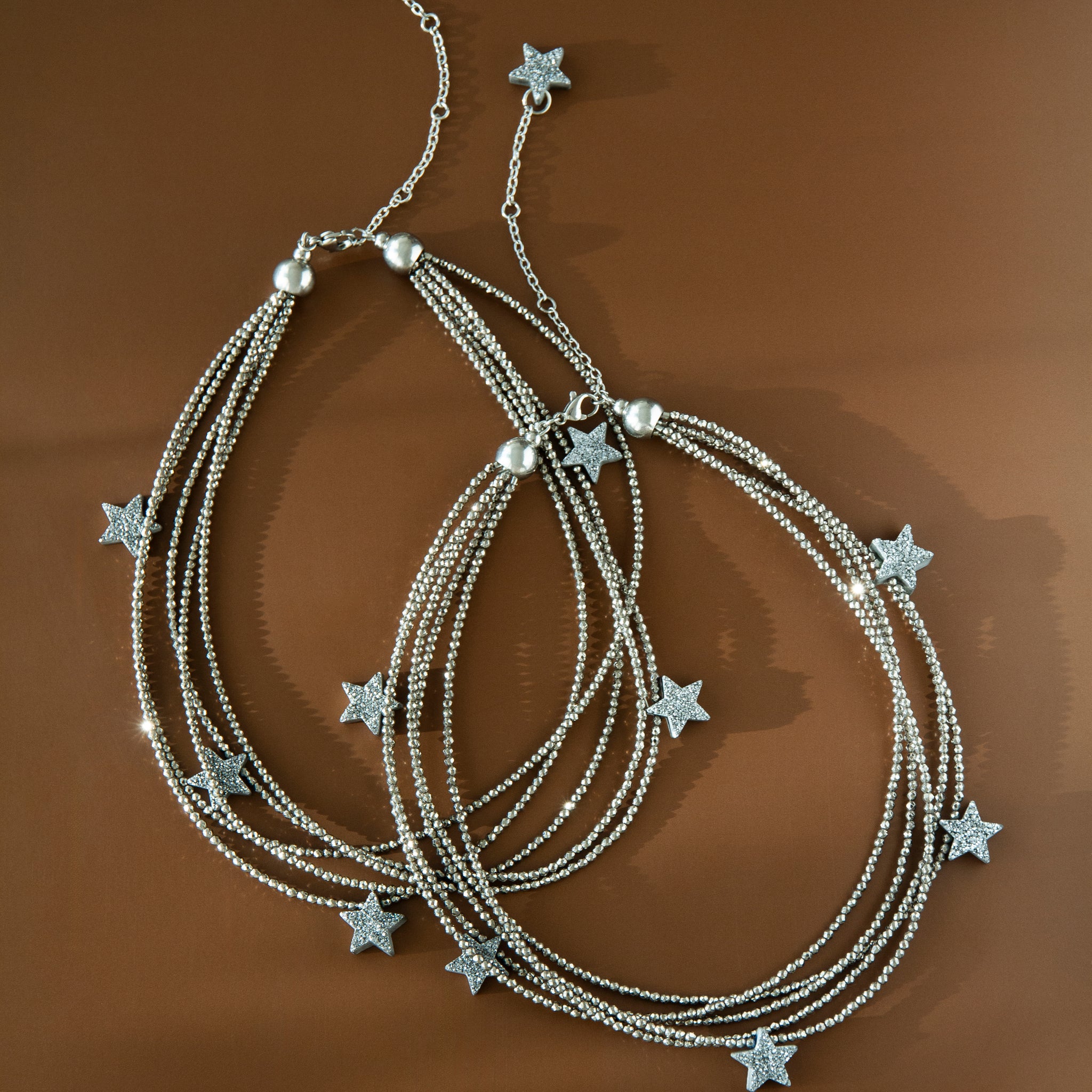 Two Make a Wish Necklaces displayed on brown background — layered hematite strands with druzy agate star charms. Modern statement jewelry styling.