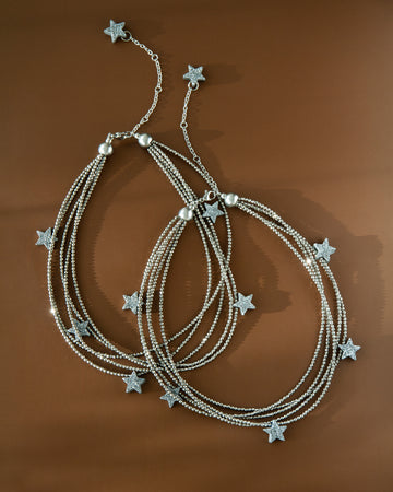 Two Make a Wish Necklaces displayed on brown background — layered hematite strands with druzy agate star charms. Modern statement jewelry styling.