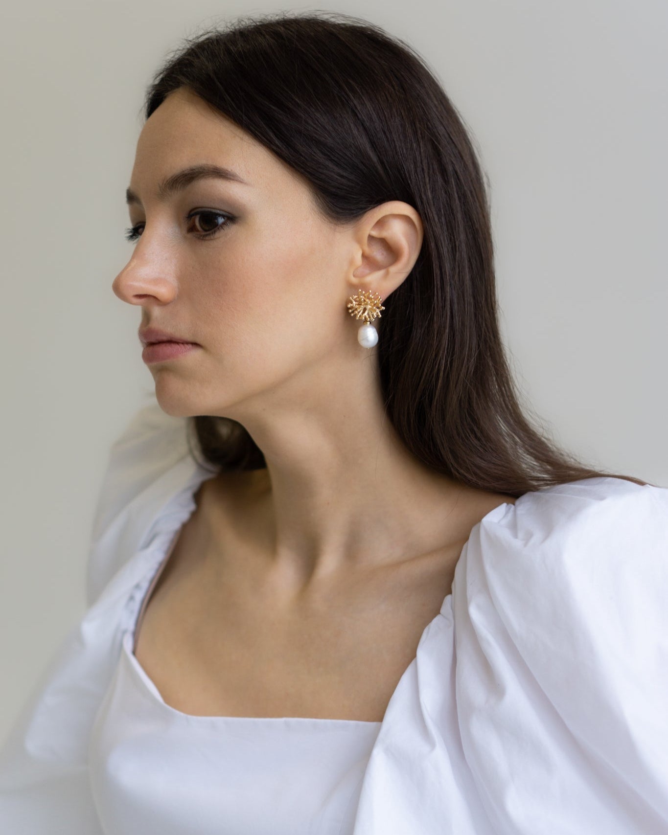 Portrait of model wearing Mermaid’s Secret Earrings — gold coral-inspired studs with baroque pearls, capturing sculptural beauty and quiet radiance.