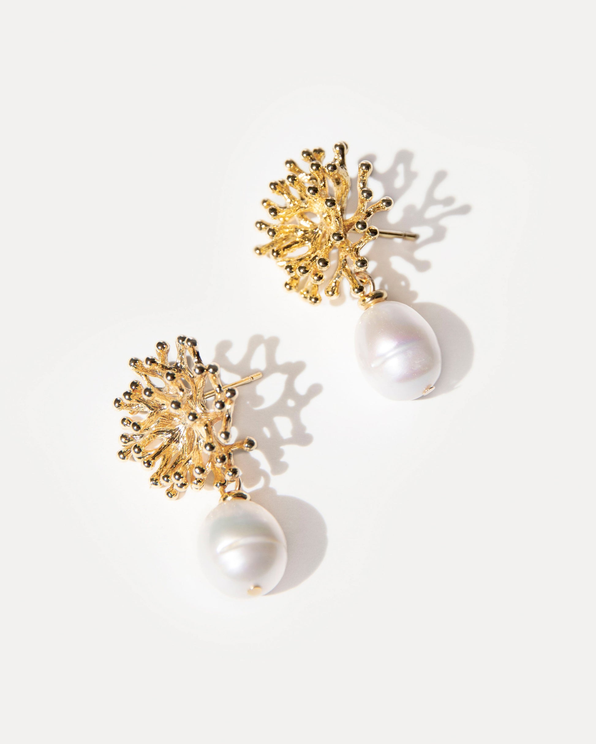 Mermaid’s Secret Earrings — flatlay of gold coral-textured studs with baroque pearls, glowing softly in natural light, elegant and ocean-inspired.