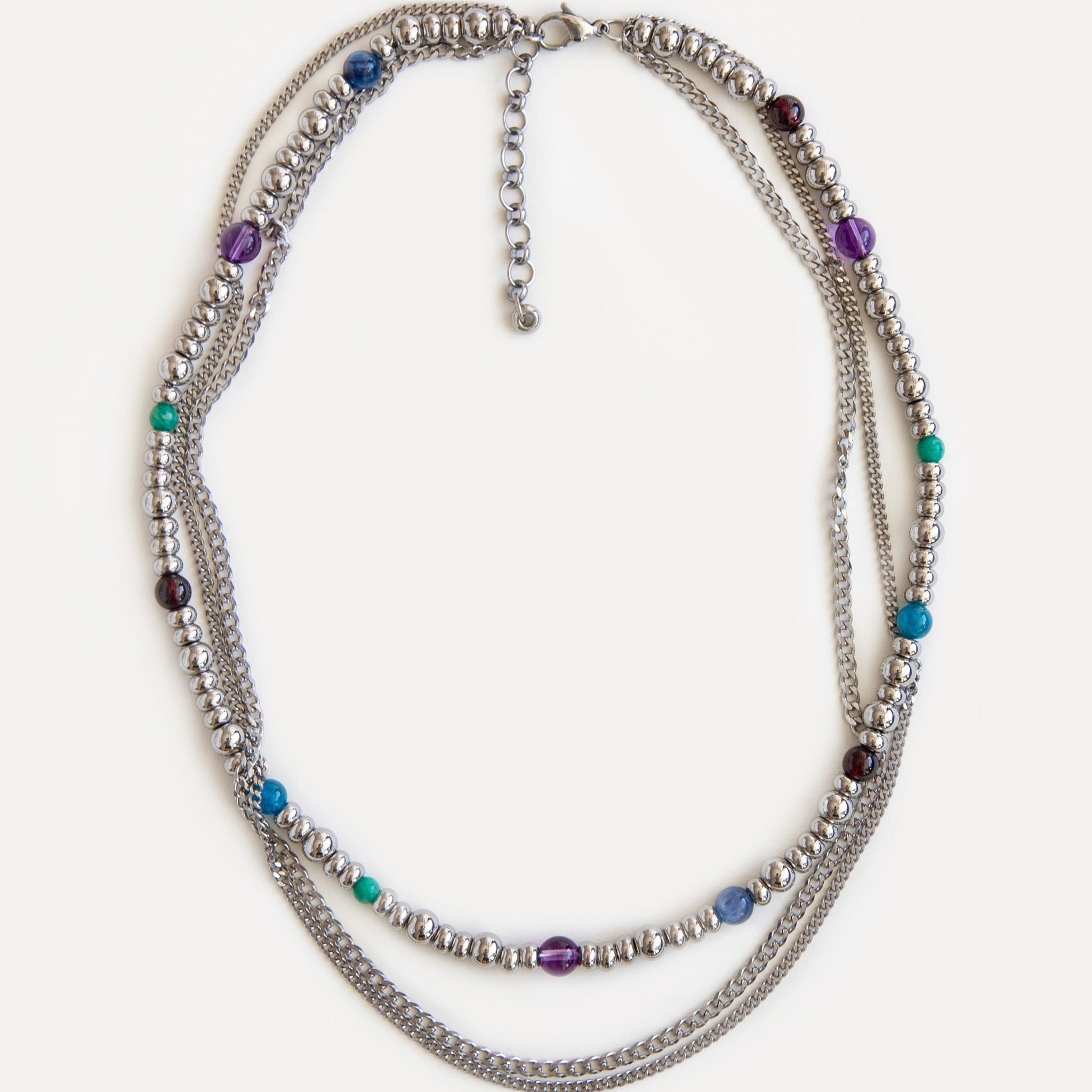 Full view of the GEMS necklace, a sophisticated three-layer design of durable jewelry steel chains and vibrant natural gemstones: garnet, amethyst, kyanite, amazonite, and apatite. Laid flat, the necklace displays its elegant symmetry and playful color combination, making it a versatile statement piece for any wardrobe. Explore Jewell Reef's unique, handcrafted fashion jewelry, perfect for layering or as a standalone gift.